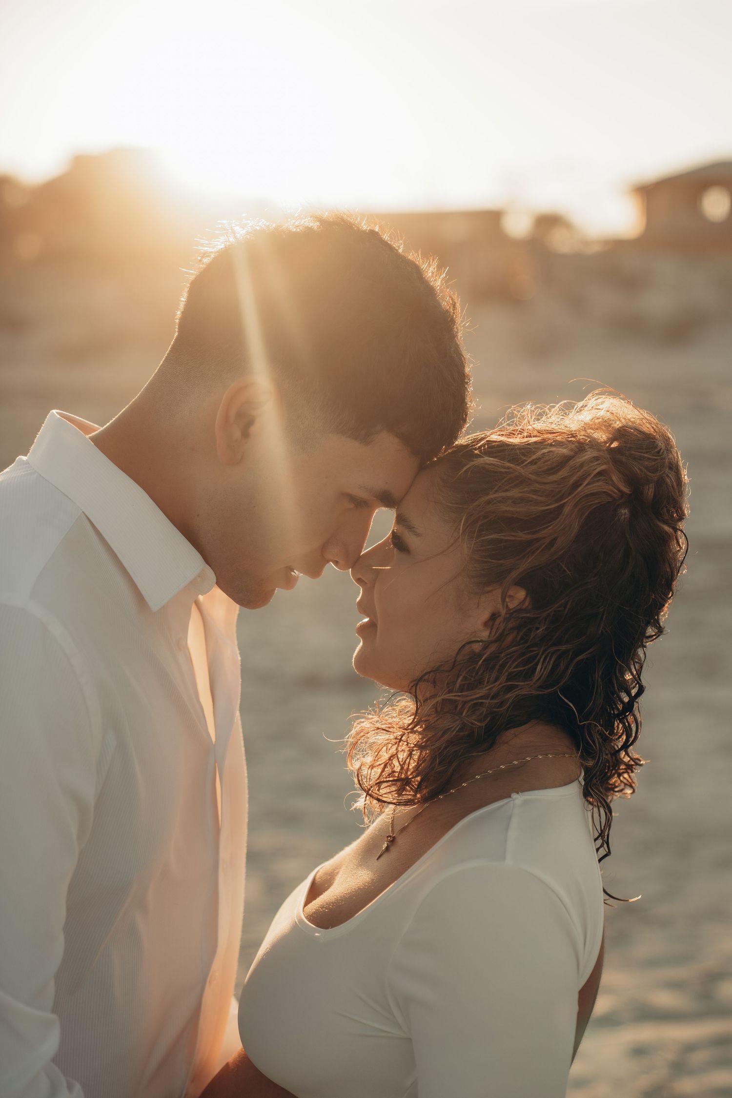 Golden hour maternity photos showing intimate moments between a couple on the beach.