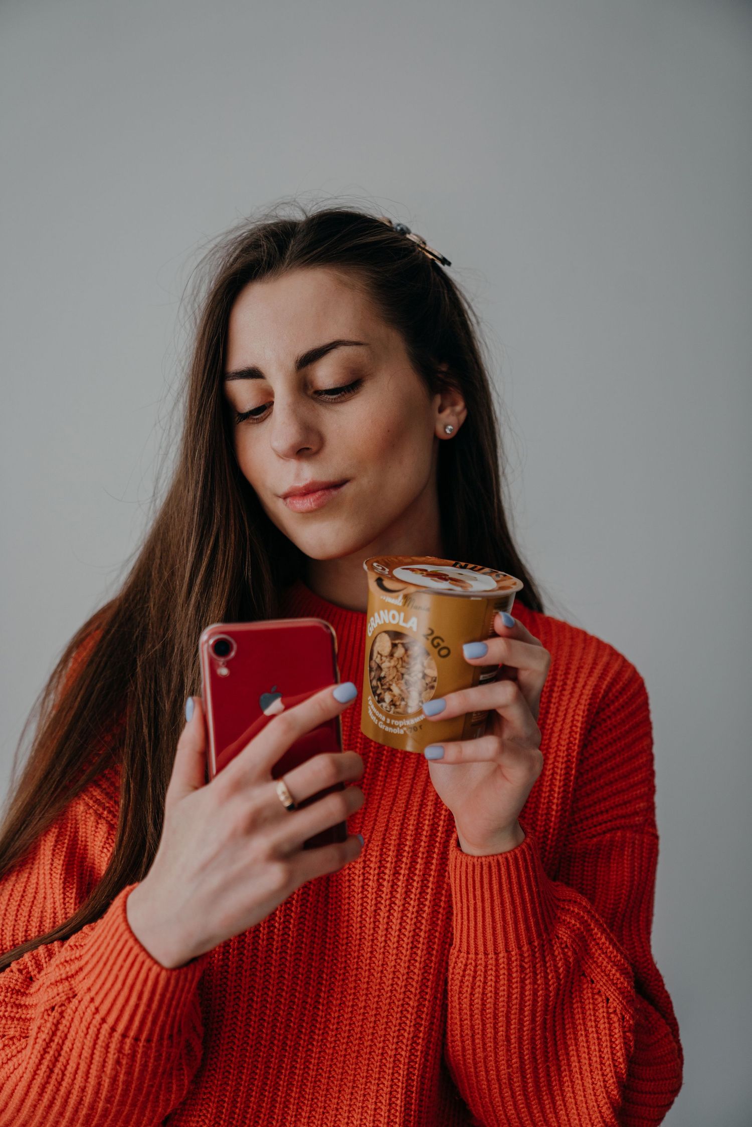 Woman in red sweater holding phone and MuesliMania muesli cup.