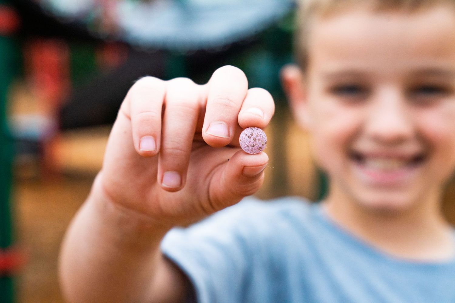 Smiling boy holding up a small vitamin gummy between his fingers outdoors.