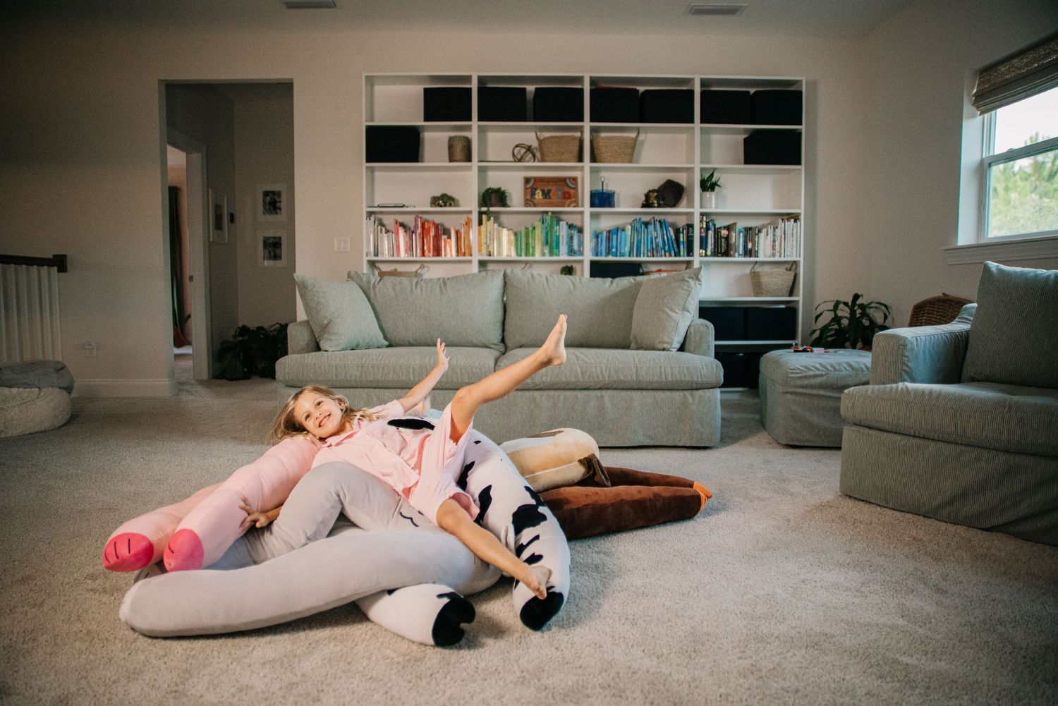 Two children playing and relaxing on carpet in bright living room with bookshelves.
