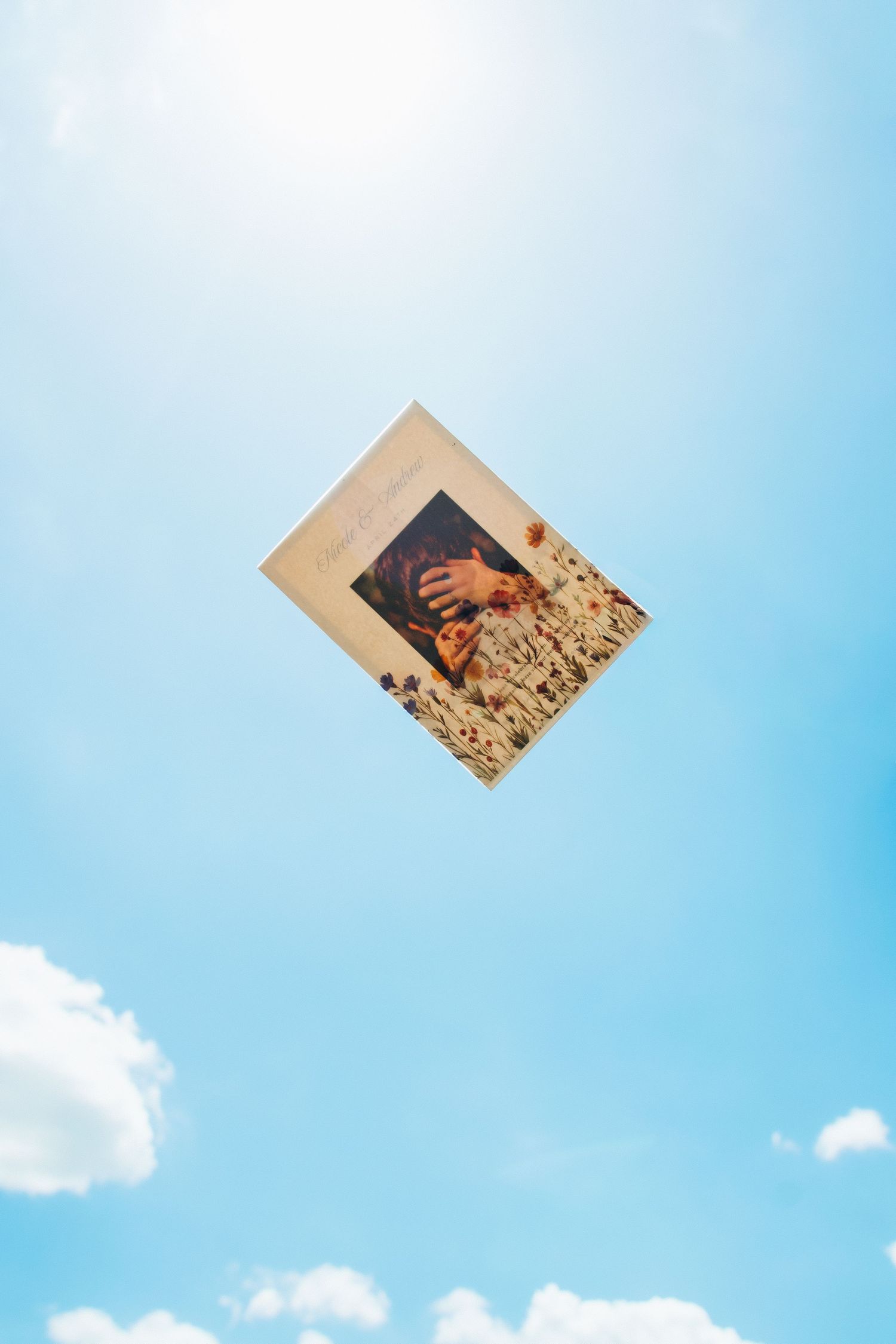 A book with a floral cover photo floats against a bright blue sky with white clouds.
