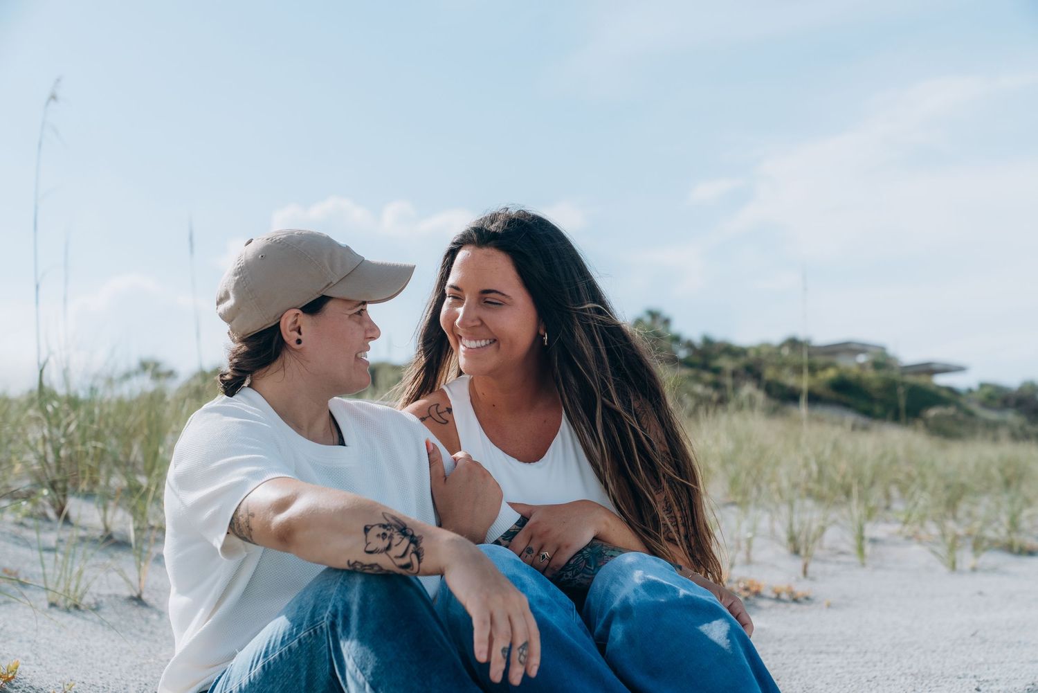 Two people sharing intimate moments on a sandy beach with dunes in the background.