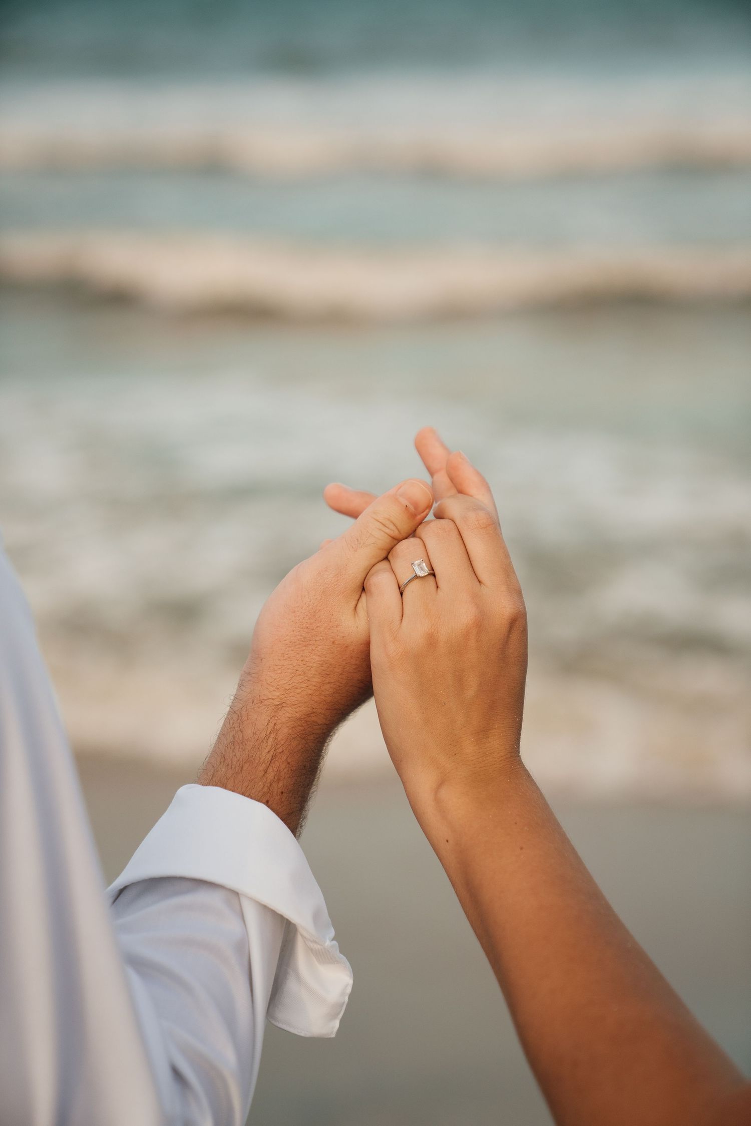 Close-up of hands with engagement ring against an ocean backdrop.