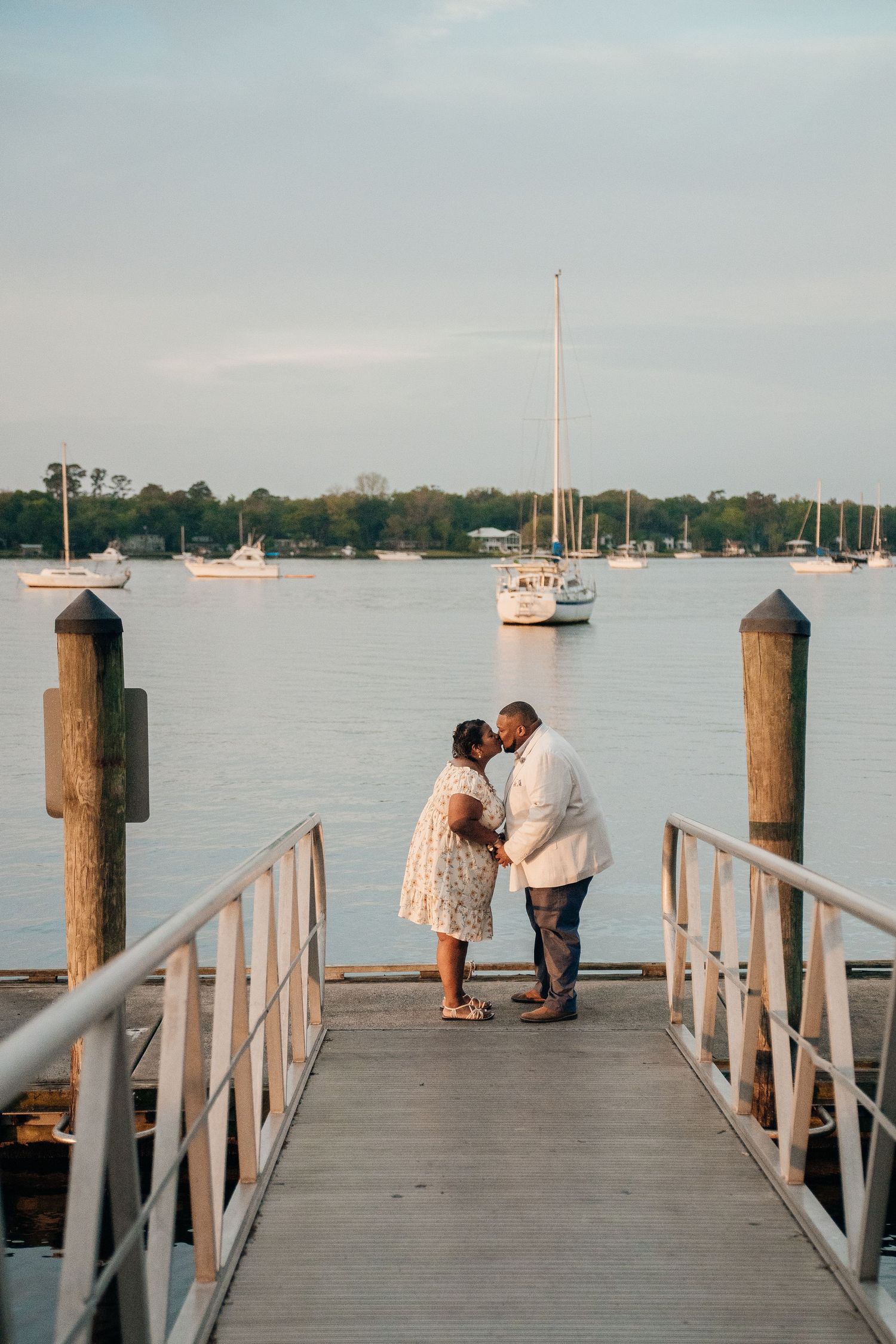 Romantic sunset photoshoot on a wooden dock with boats in the background.