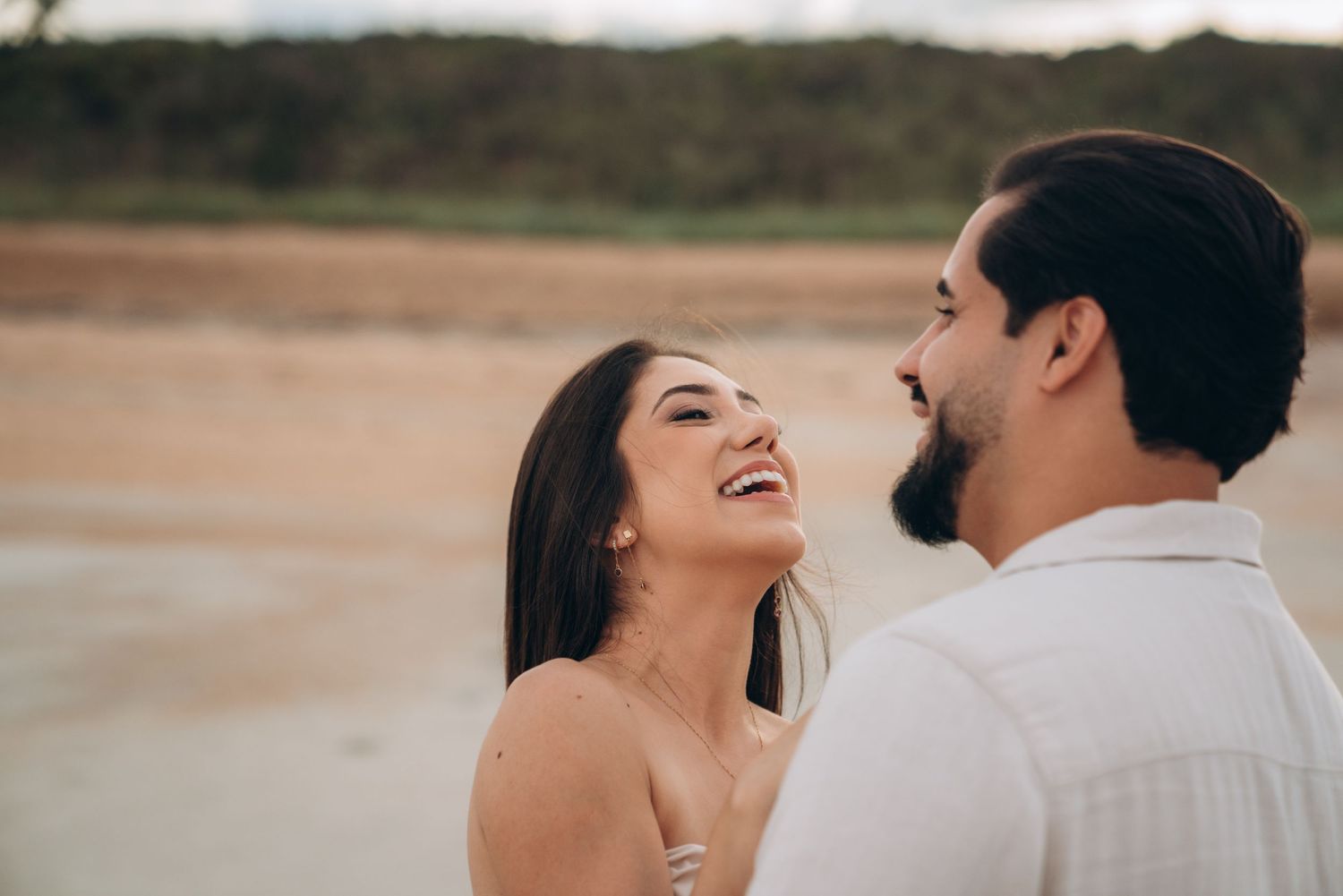 A couple sharing joyful laughter while embracing on a beach during golden hour.