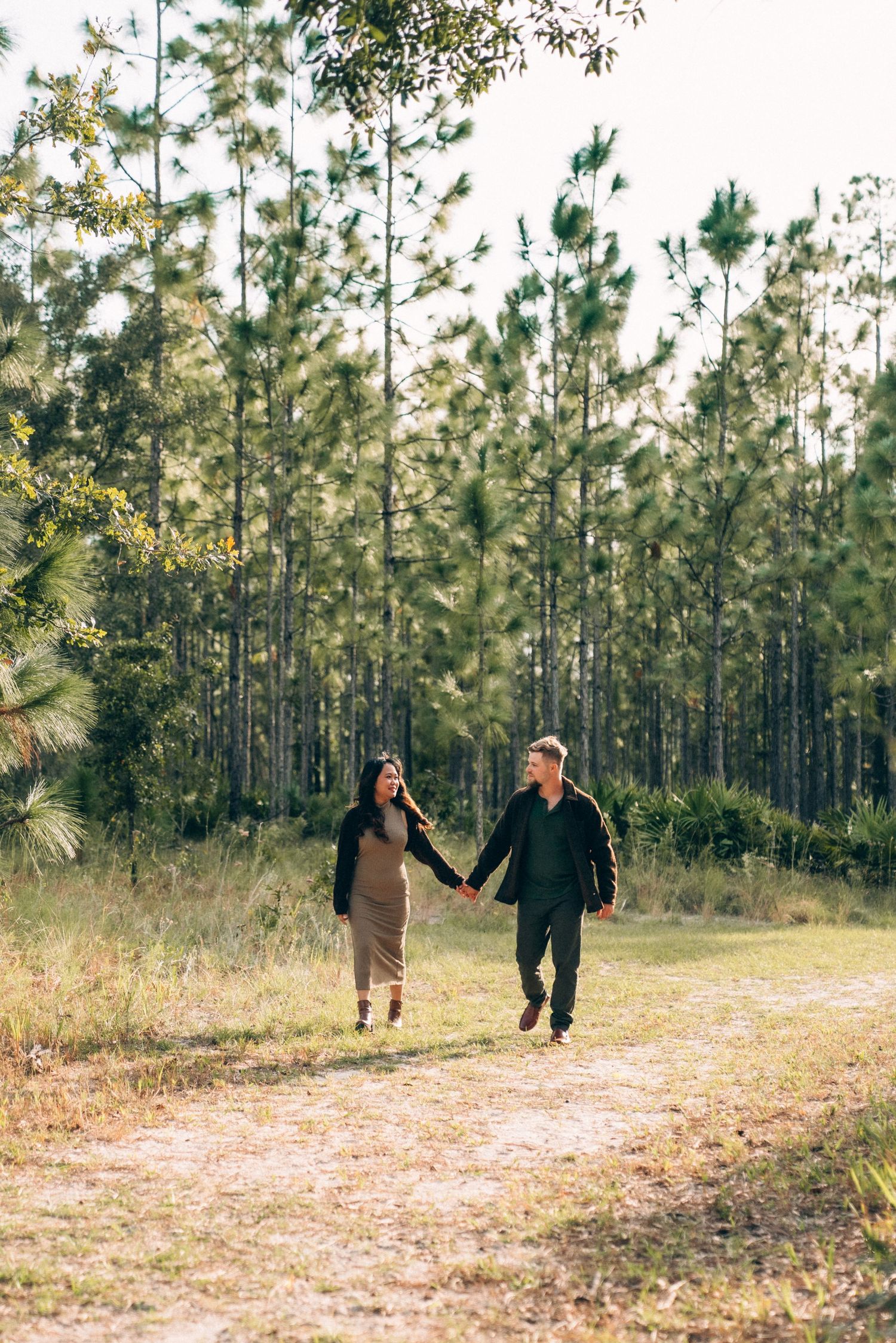 Couple playfully runs through a pine forest clearing during a photo session.