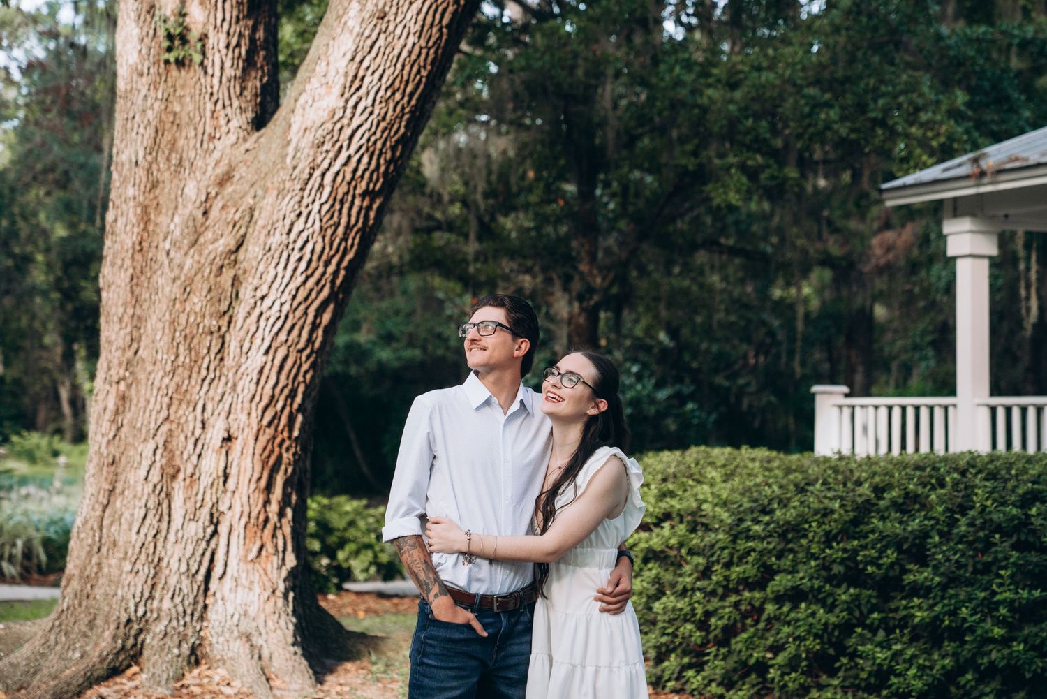Romantic couple shares tender moments under majestic oak trees in a scenic garden setting.