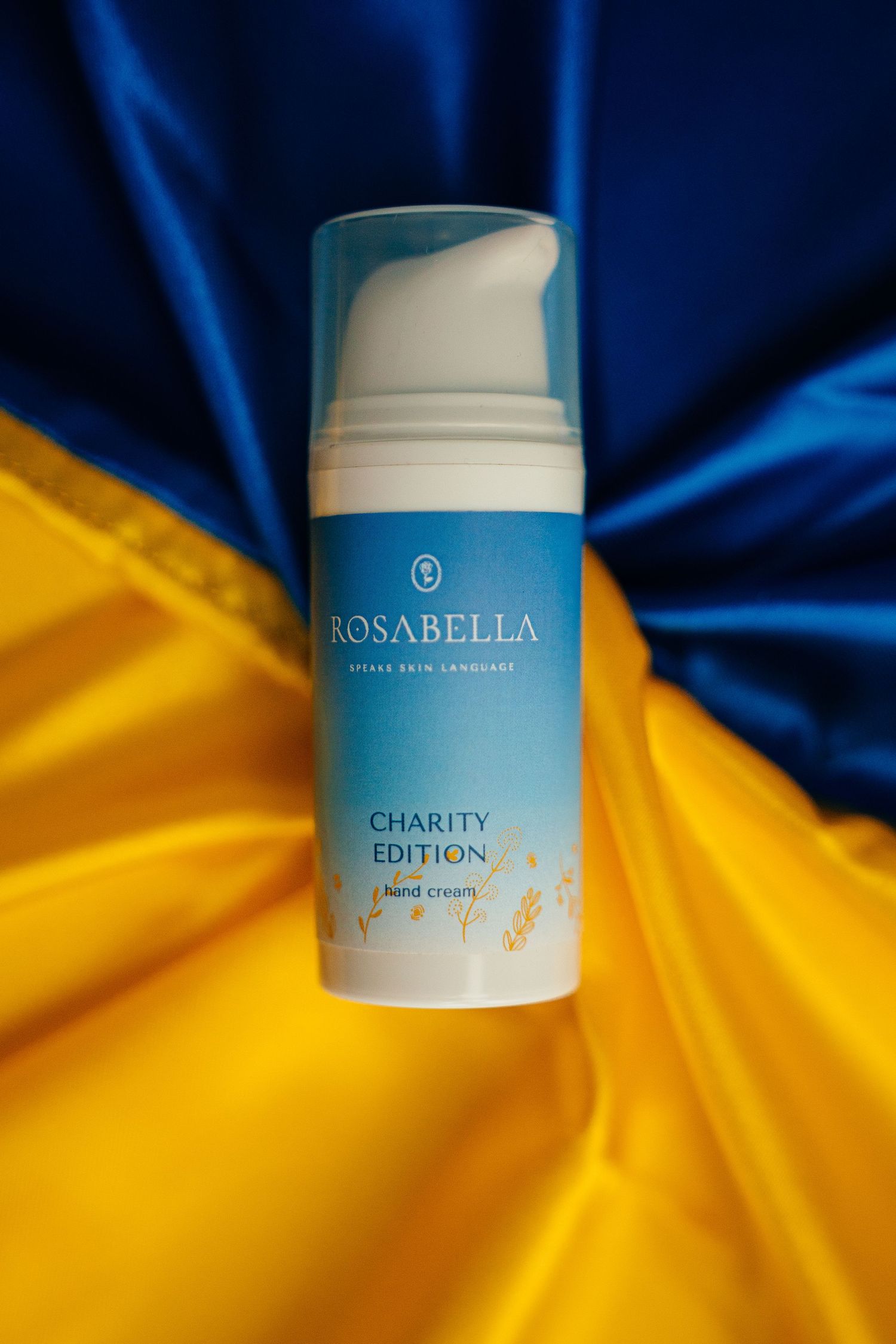 Rosabella Charity Edition hand cream bottle displayed on Ukrainian blue and yellow flag.