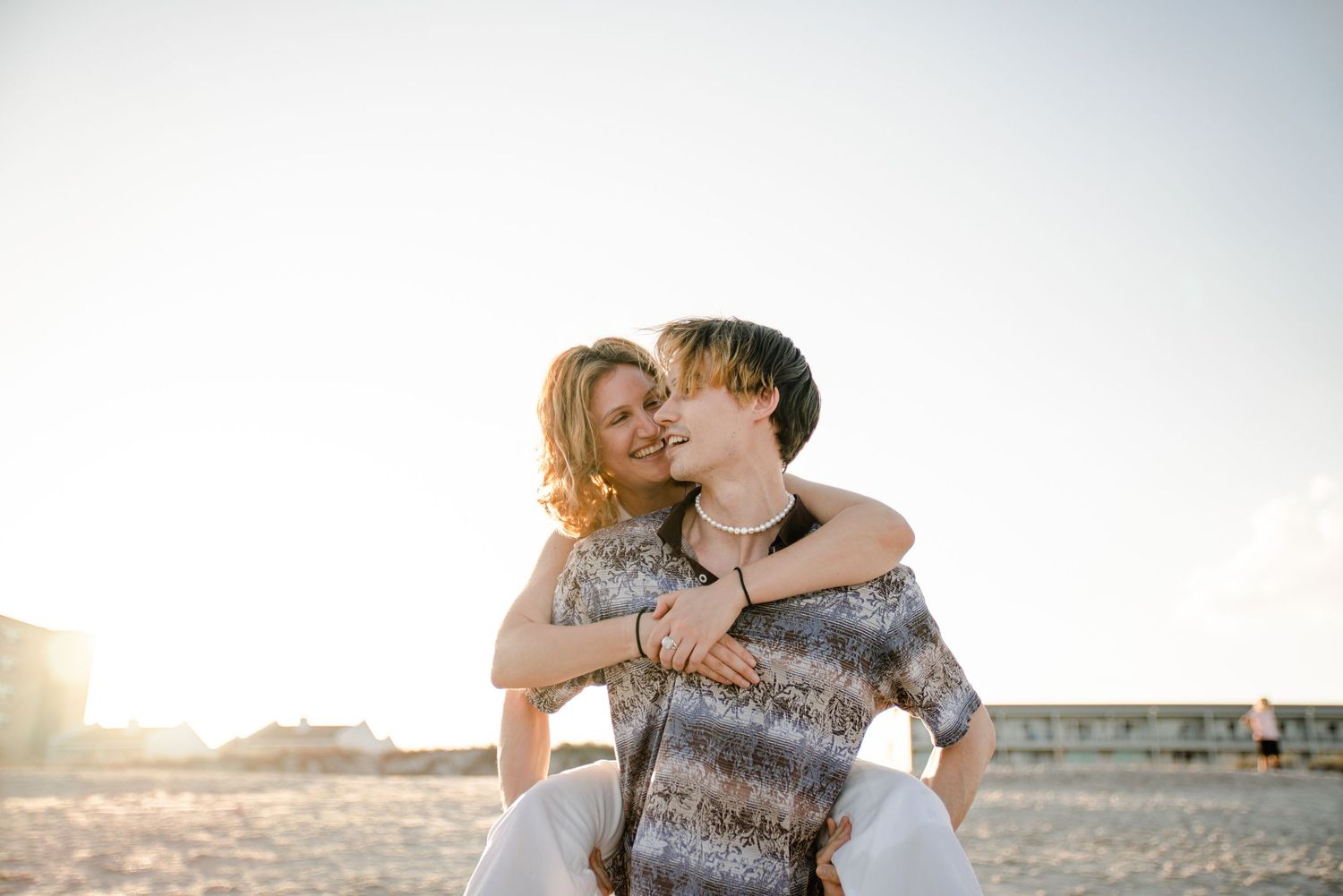 A romantic couple embraces and laughs together in soft sunlit portraits at sunset.