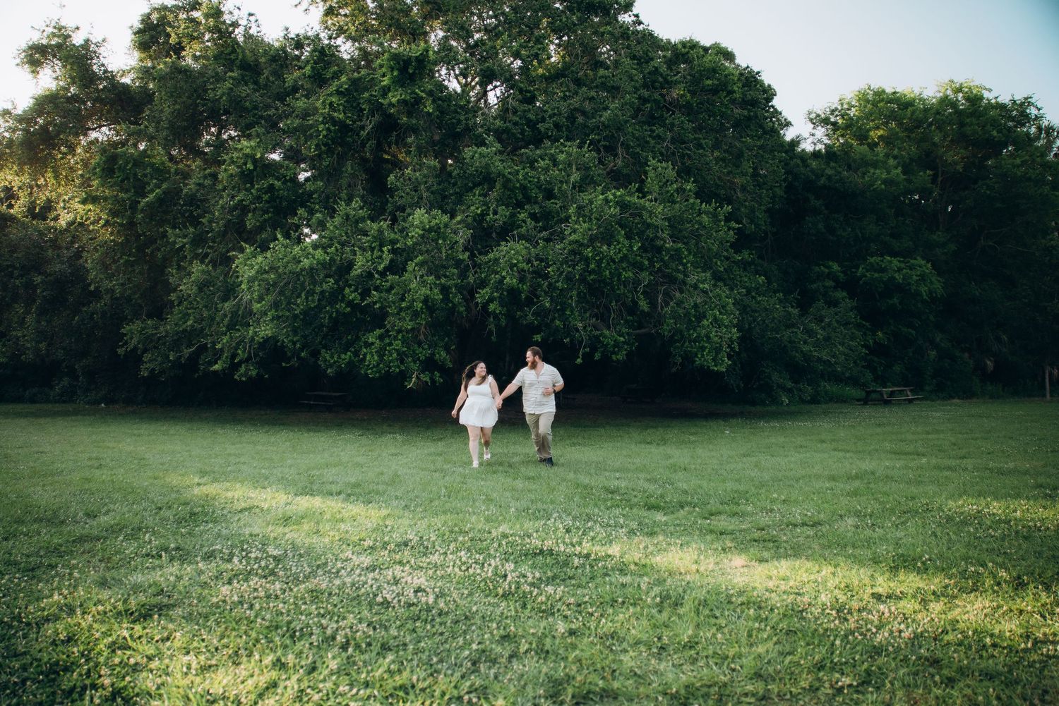 Panoramic view of a green field with trees and two people in the distance.