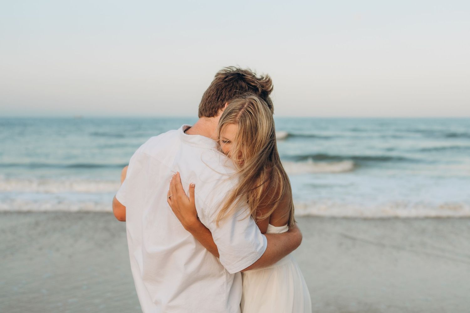 A romantic couple shares an intimate moment on the beach with ocean waves in the background.