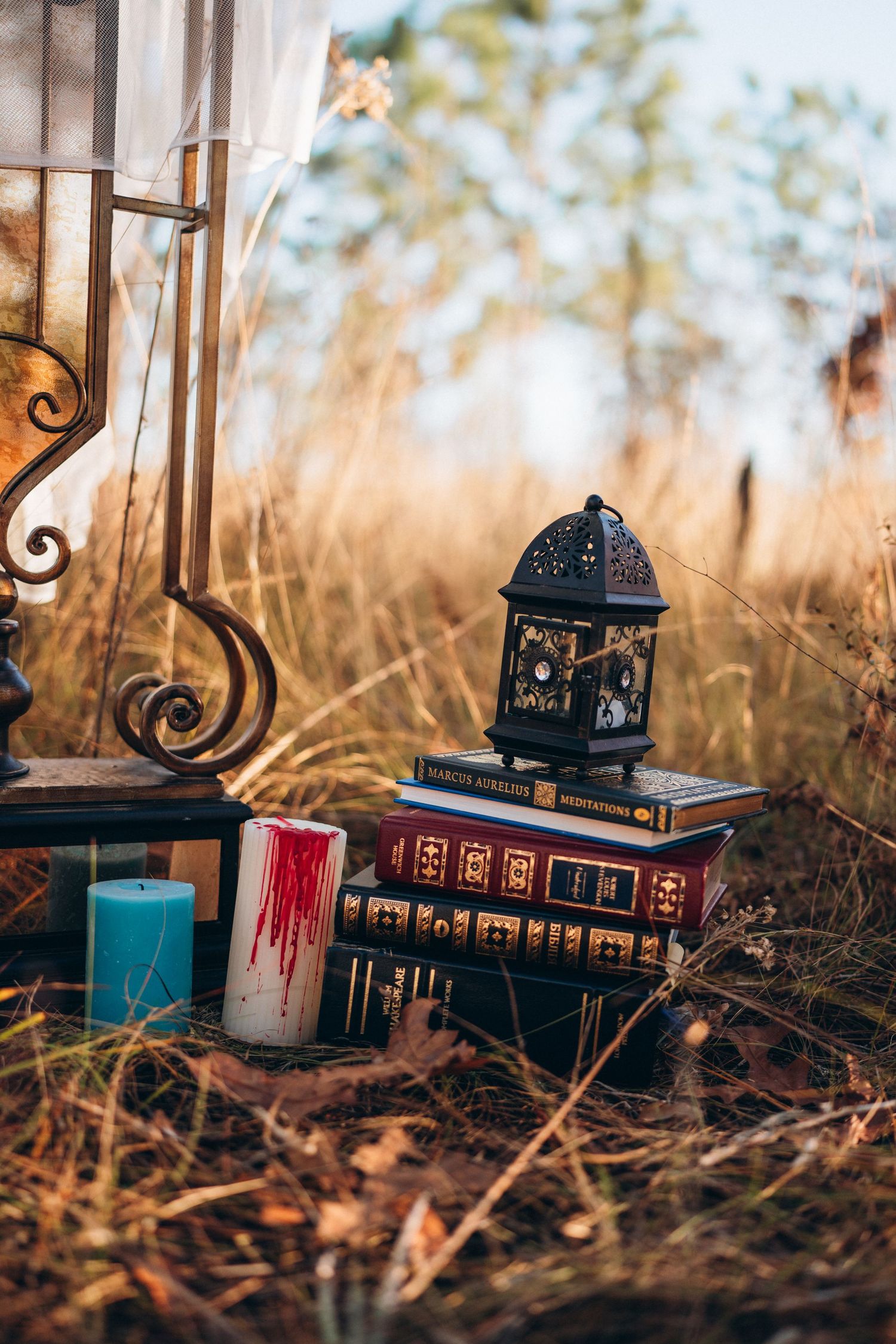 Stack of antique books with decorative lantern and candles in autumn field setting.