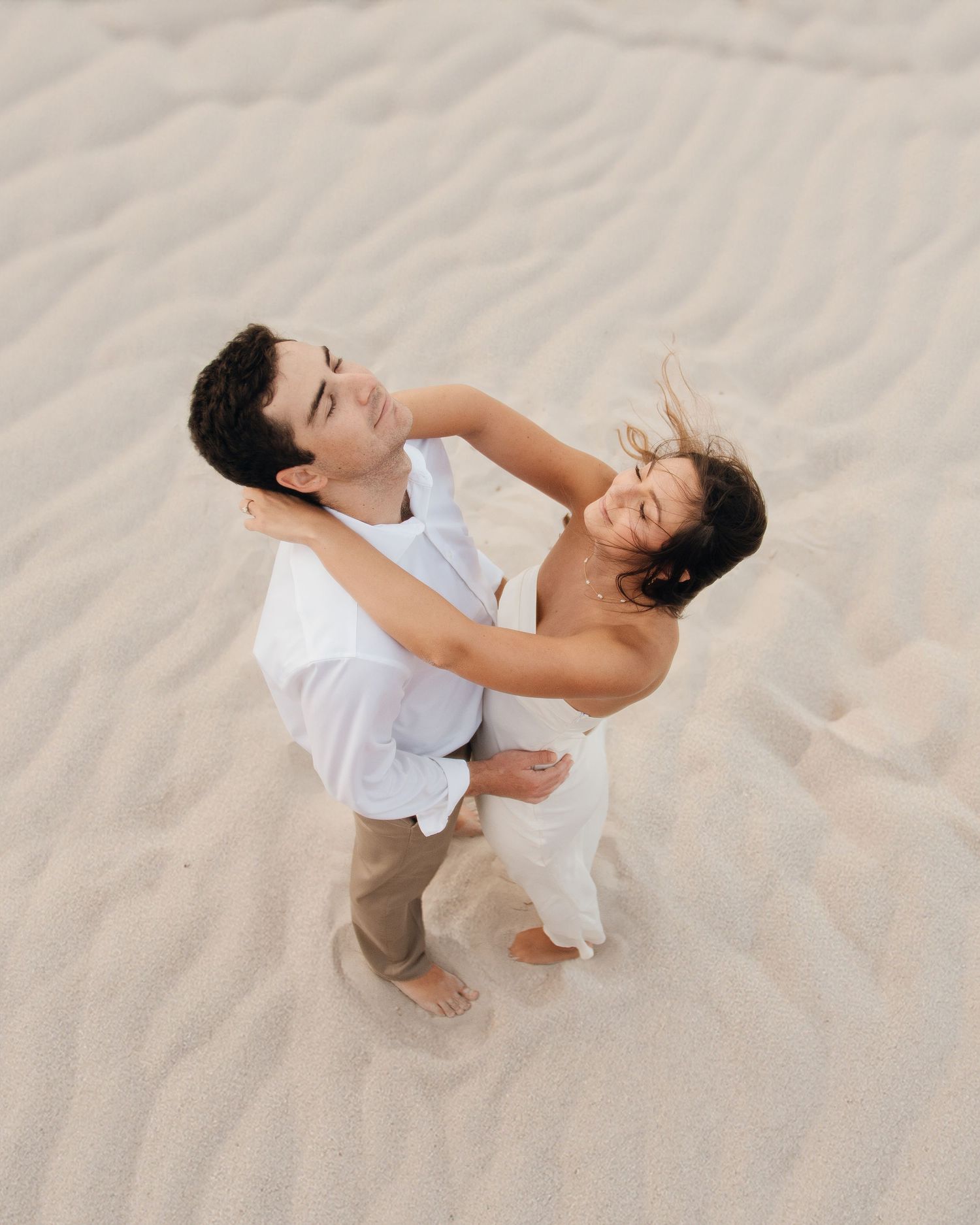 Aerial shot of a couple dancing and laughing on beach sand.