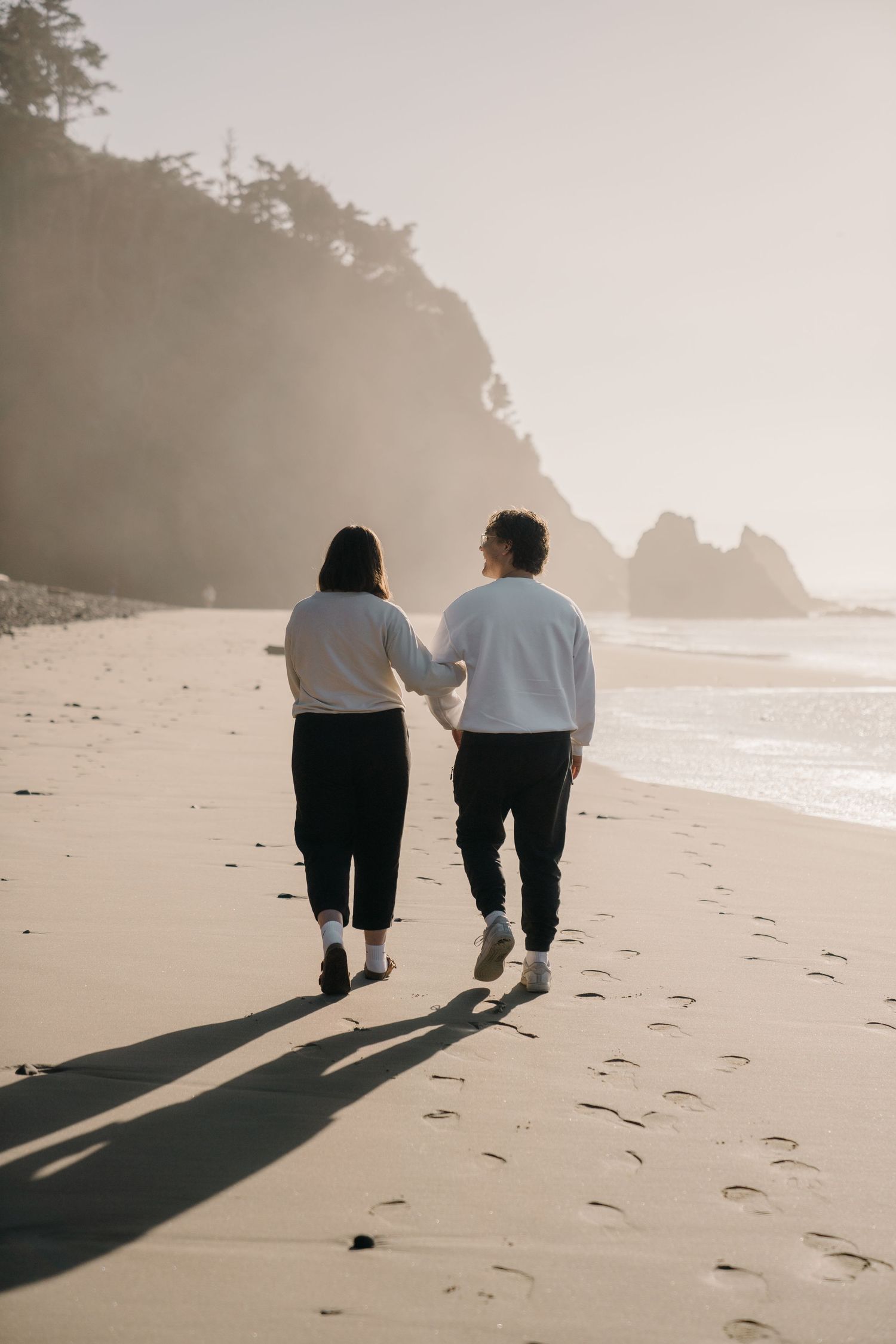 A couple walking together on a misty beach leaving footprints in the sand.