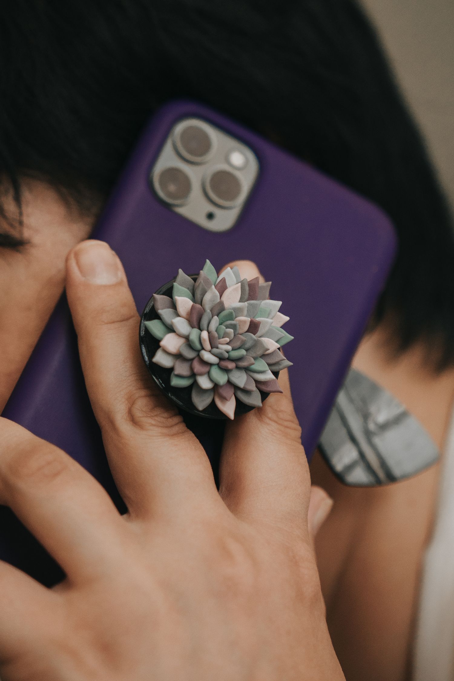Hand holding a small succulent plant against a purple iPhone case with triple camera lens.