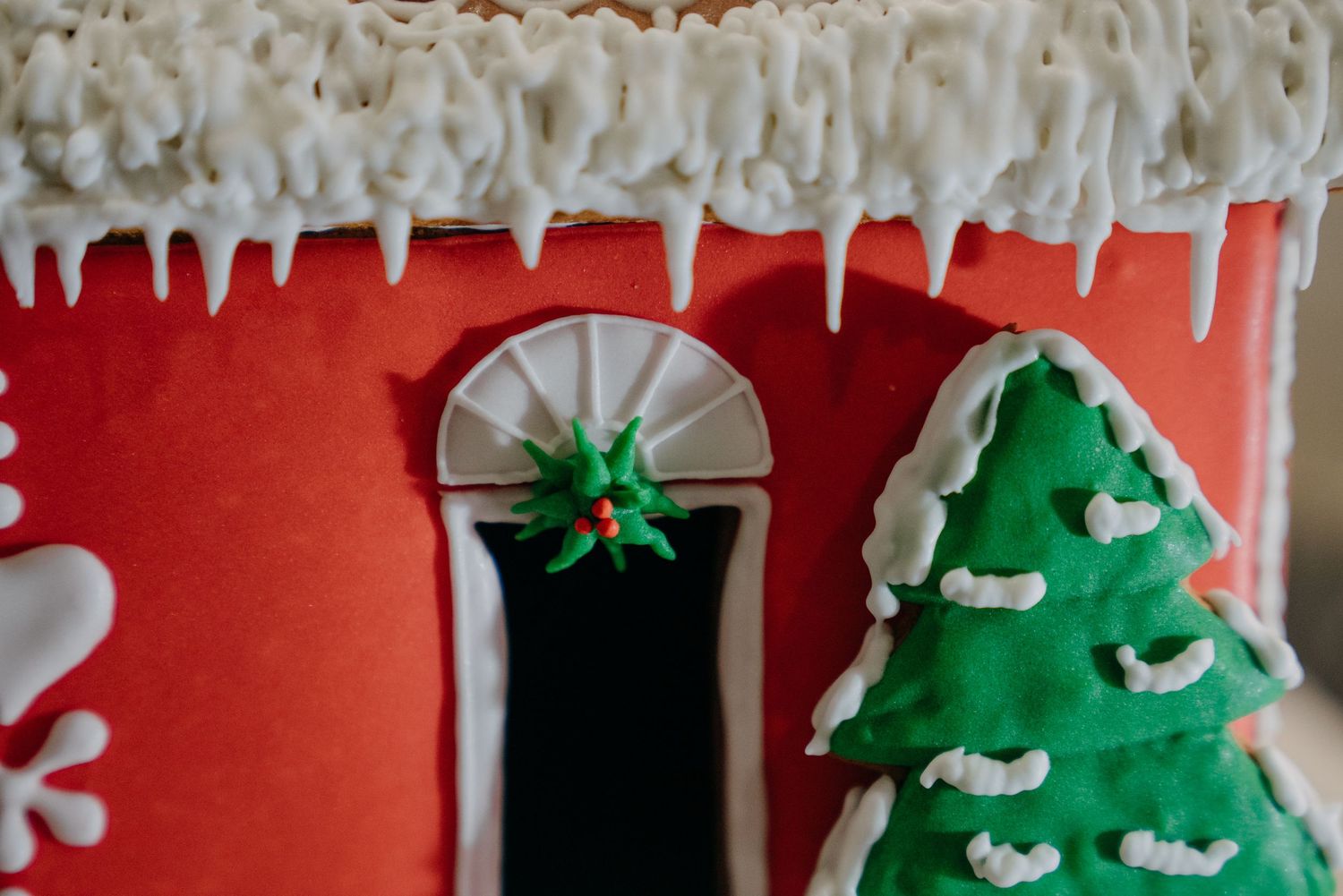 Close-up of a decorative gingerbread house with red walls, white icing icicles, and a green Christmas tree.