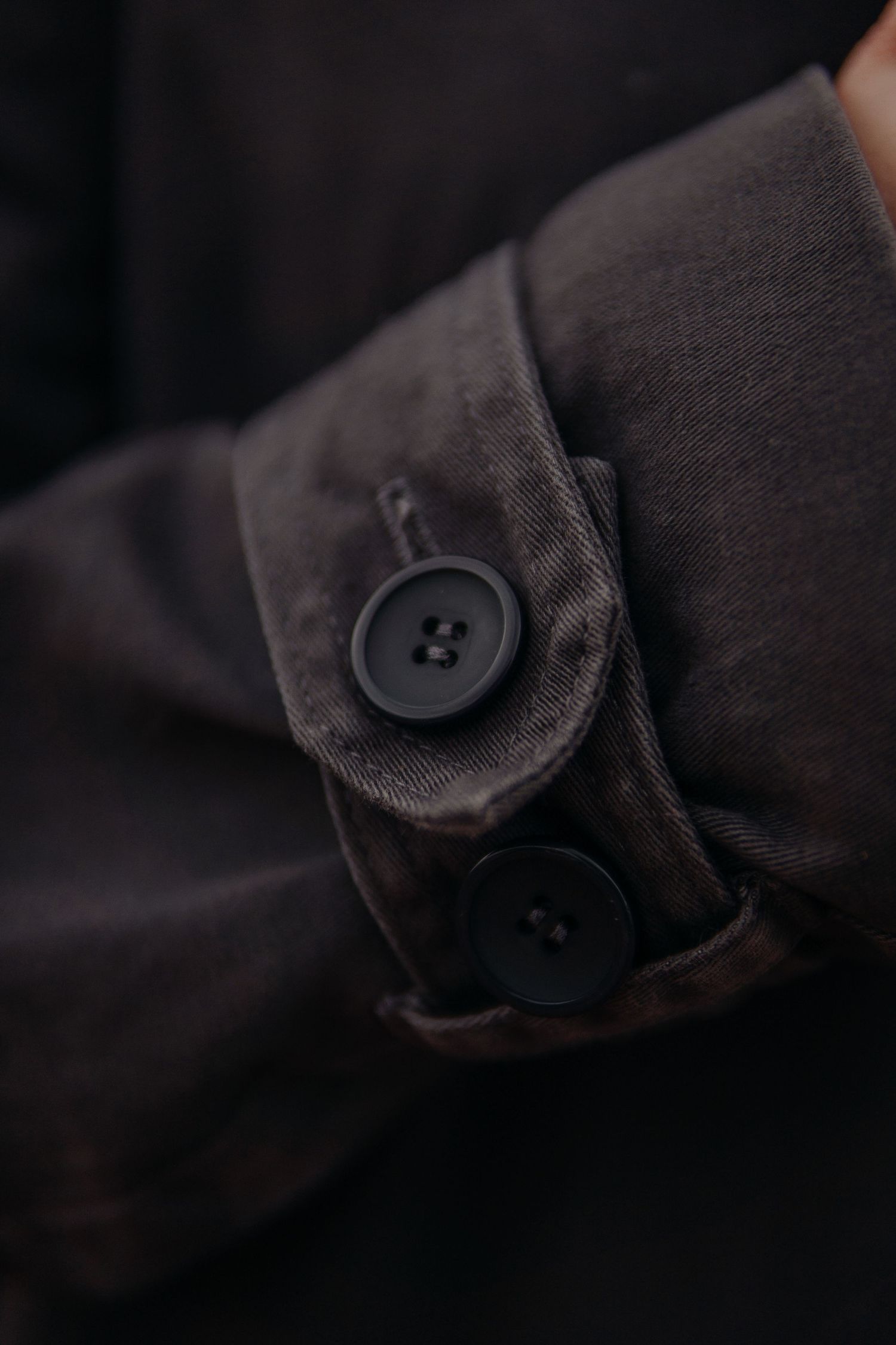 Macro close-up of dark gray jacket sleeve cuff with two black buttons on dark background.