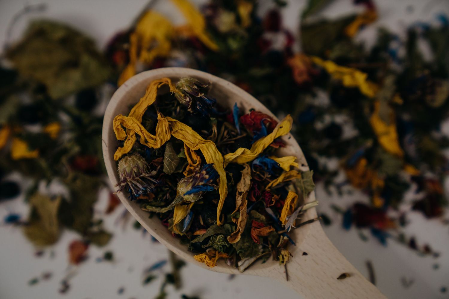A wooden spoon filled with colorful loose leaf herbal tea blend featuring yellow marigold petals and dried botanicals.