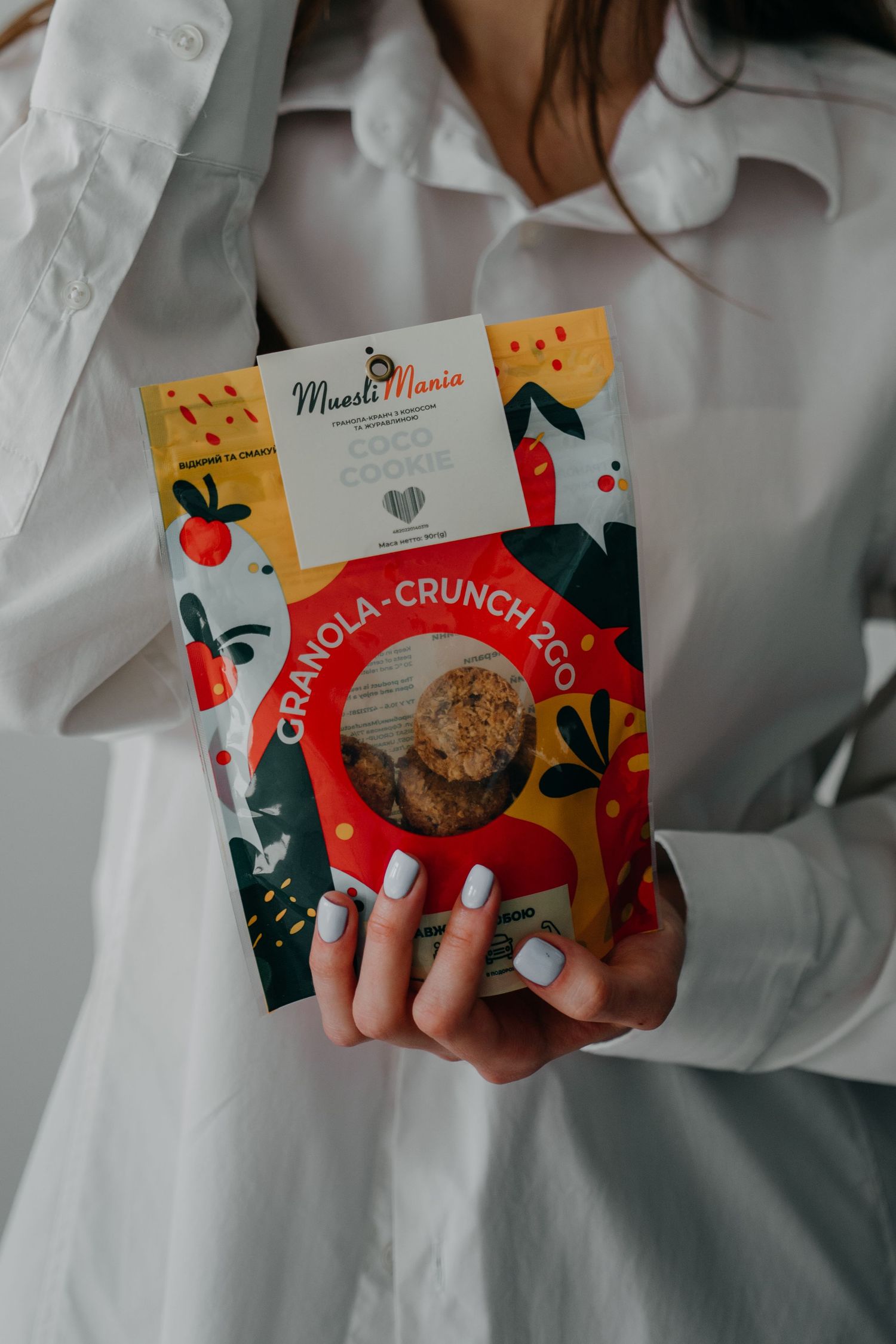 Woman in white shirt holding a colorful MuesliMania Granola-Crunch 2Go packaging.