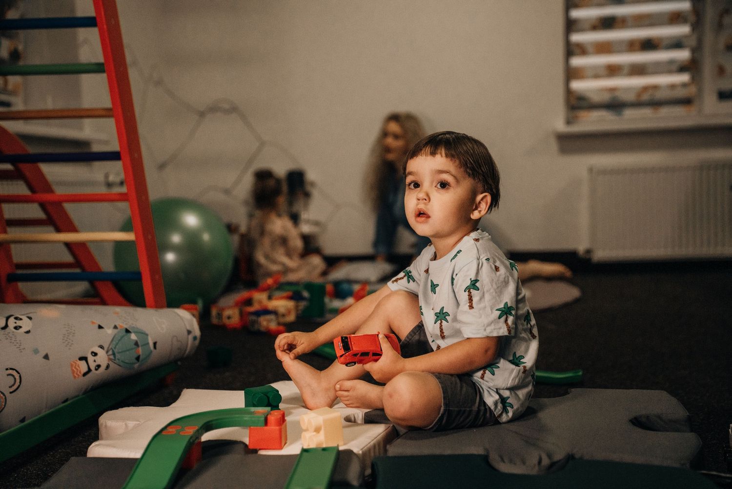 Young boy playing with colorful wooden toy blocks on a mat in a children's playroom.