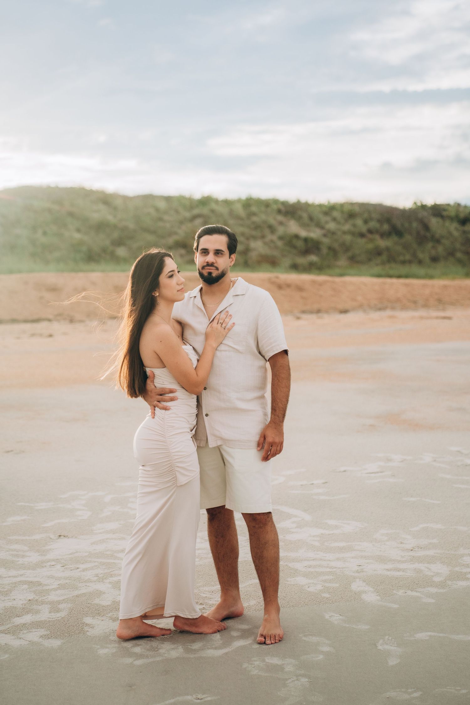 A couple in white outfits playing and laughing together in shallow ocean water.