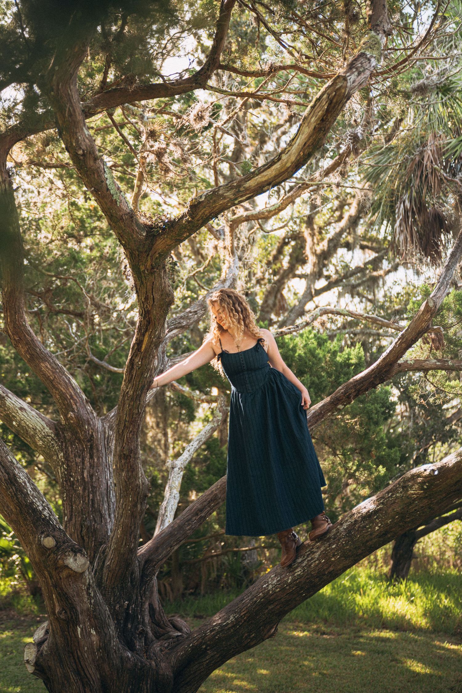 Elegant pose among tree branches in a dark navy dress.