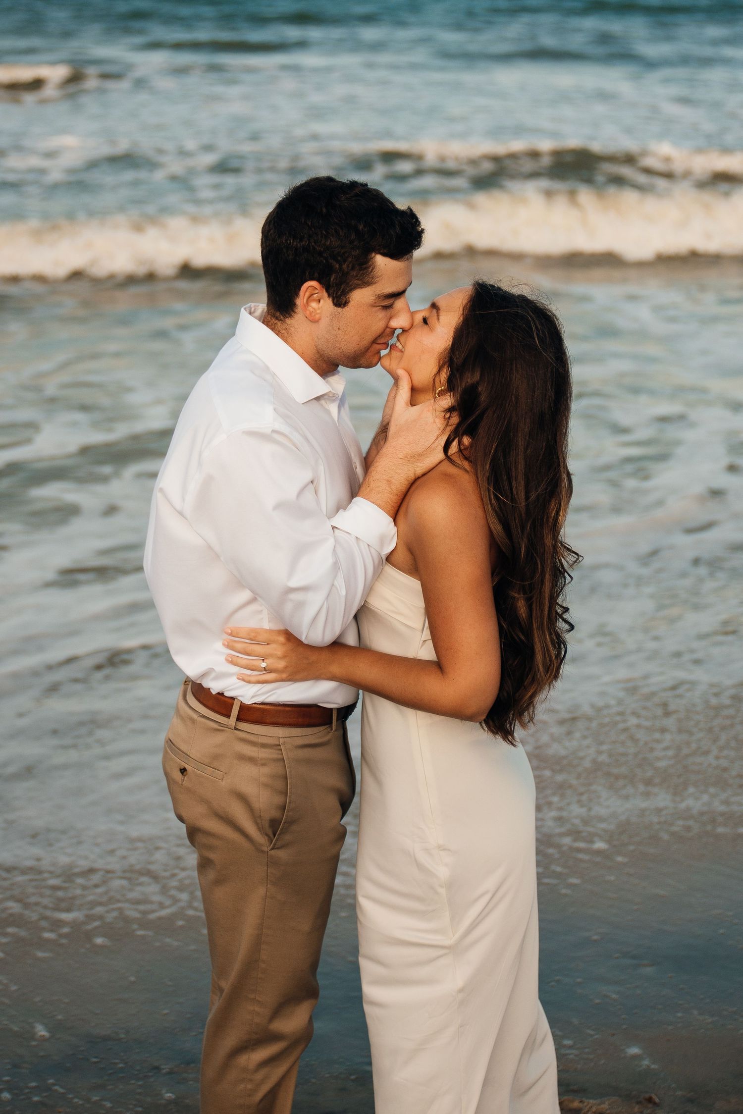 A romantic beach scene with a couple in white and tan attire sharing an intimate moment.