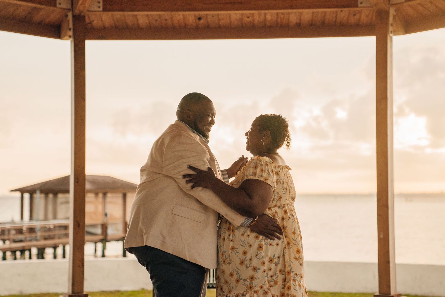 A romantic couple shares tender moments at a beachside pier during sunset.