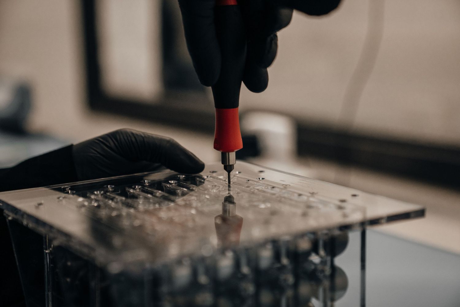 Gloved hand using a red screwdriver on a metal circuit board in a technical repair setting.