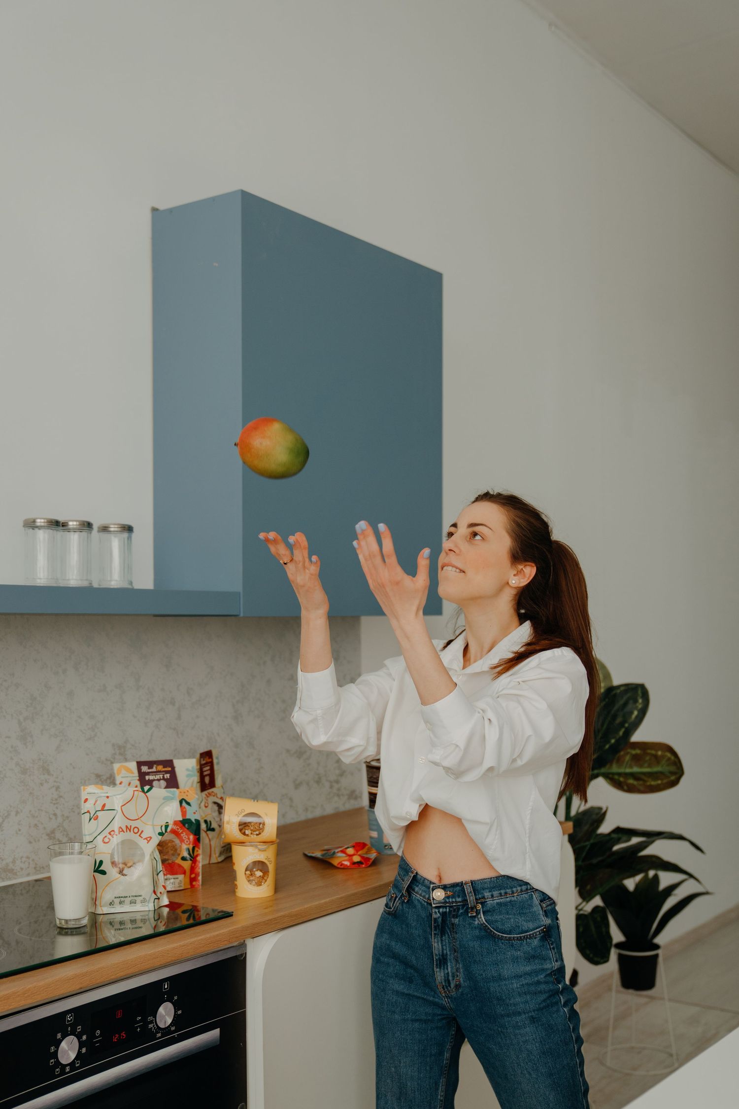 Young woman tossing a mango in a modern blue and white kitchen.