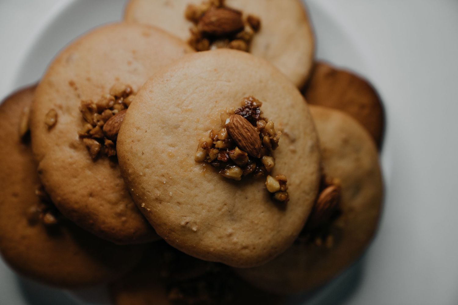Close-up of round pecan cookies topped with crunchy nut clusters on a white plate.