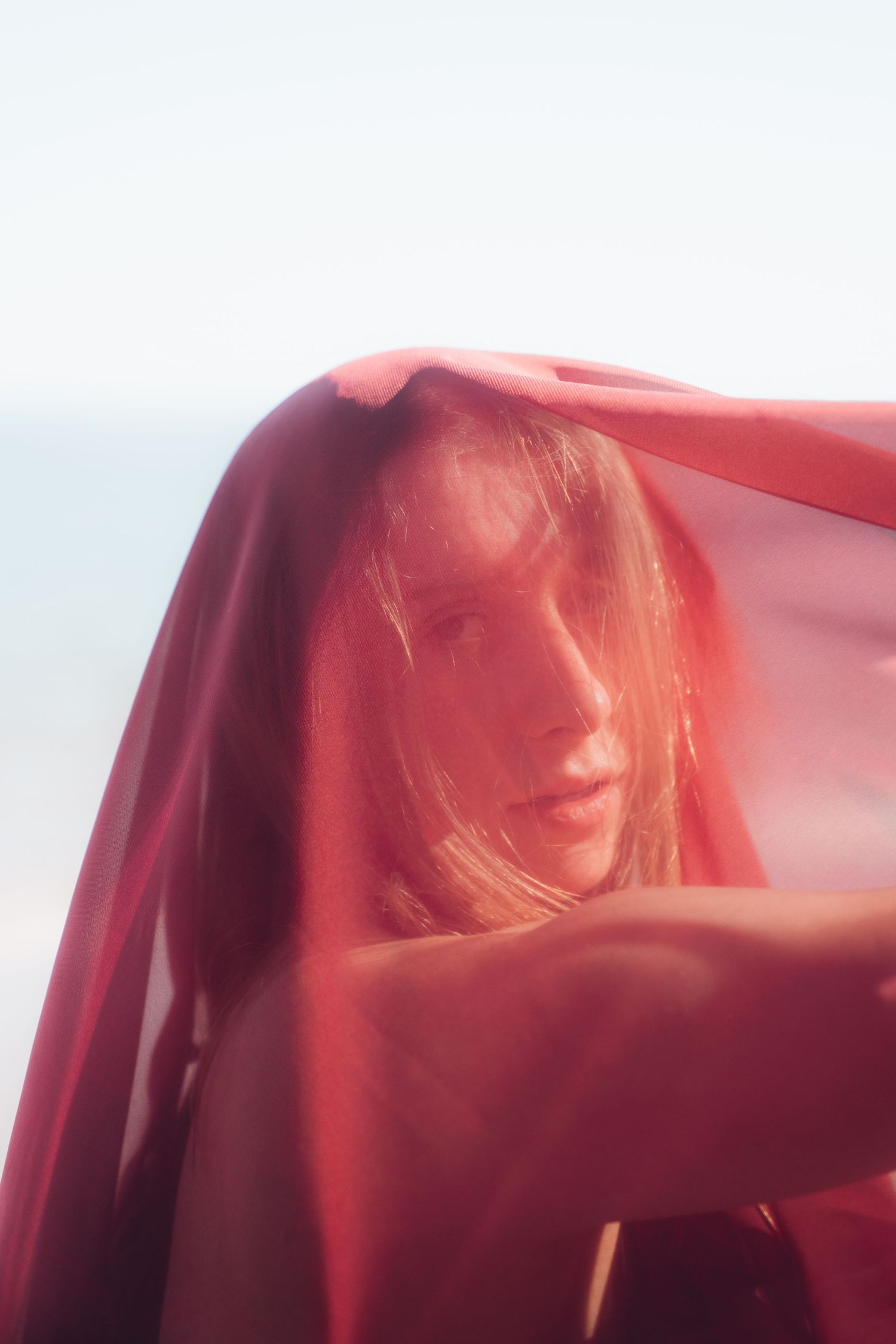 Artistic portrait series with red fabric creating an ethereal flowing effect against a light background.