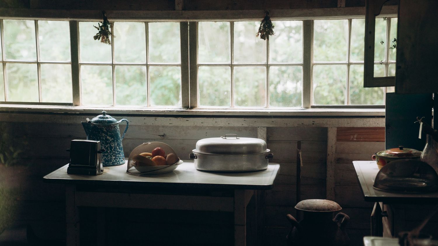 A long rustic dining table with benches sits in front of large windows in a sunlit restaurant space.