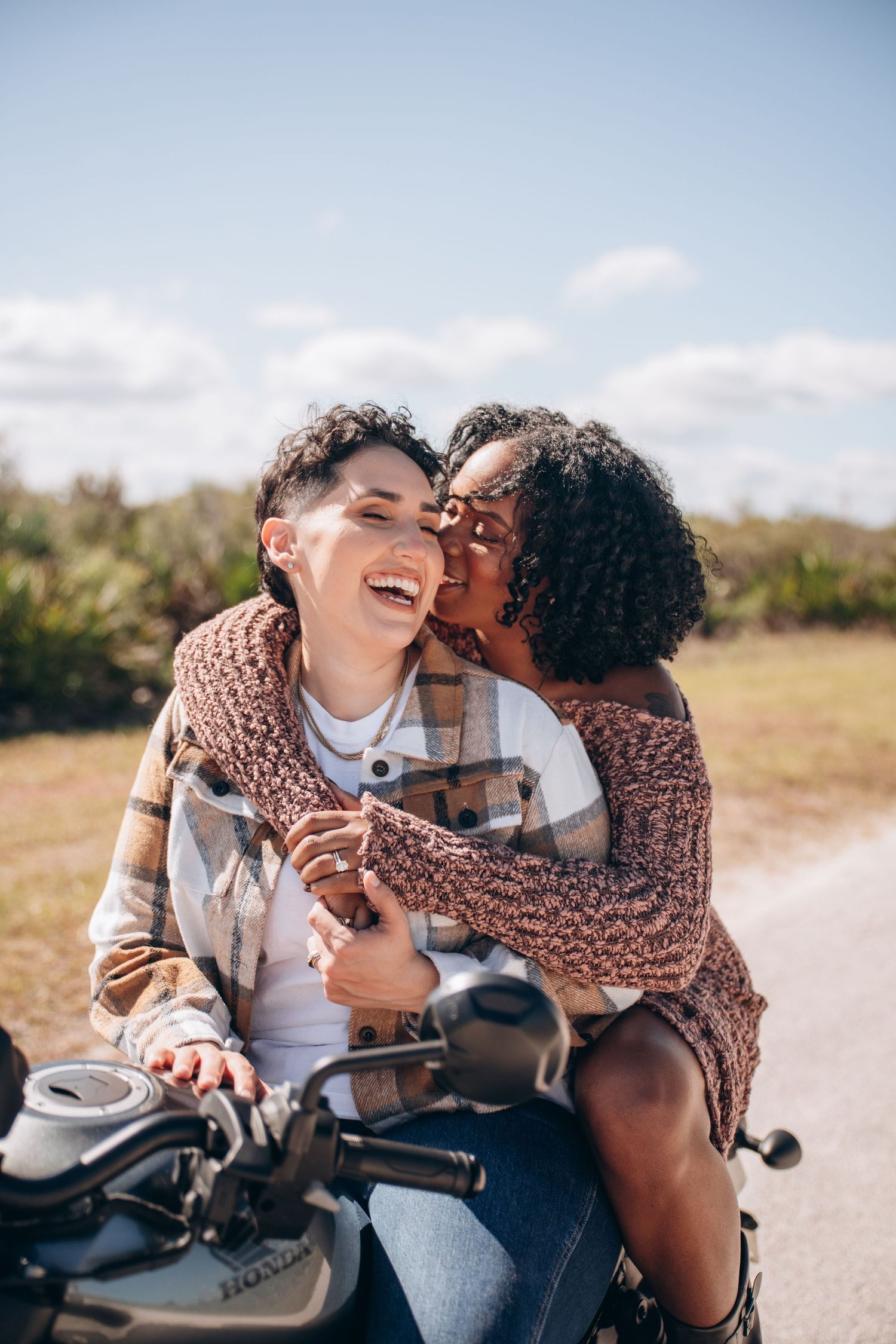 Couple shares playful moments while sitting on a motorcycle on a sunny day.