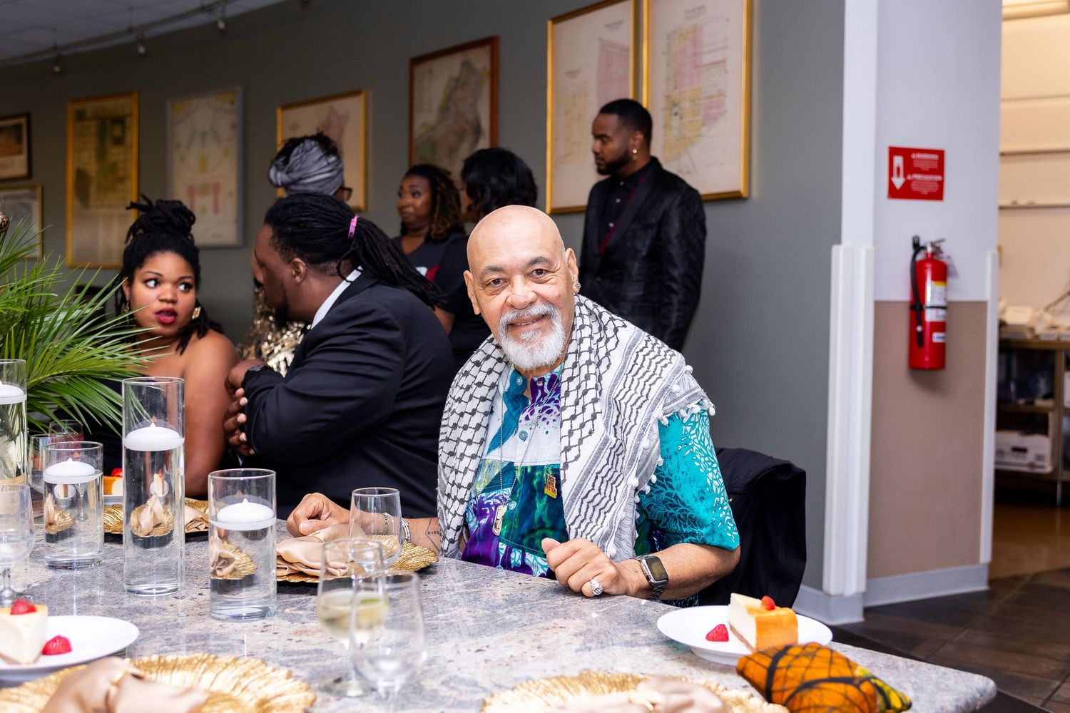 A guest smiles warmly while seated at a dining table during an indoor social gathering.