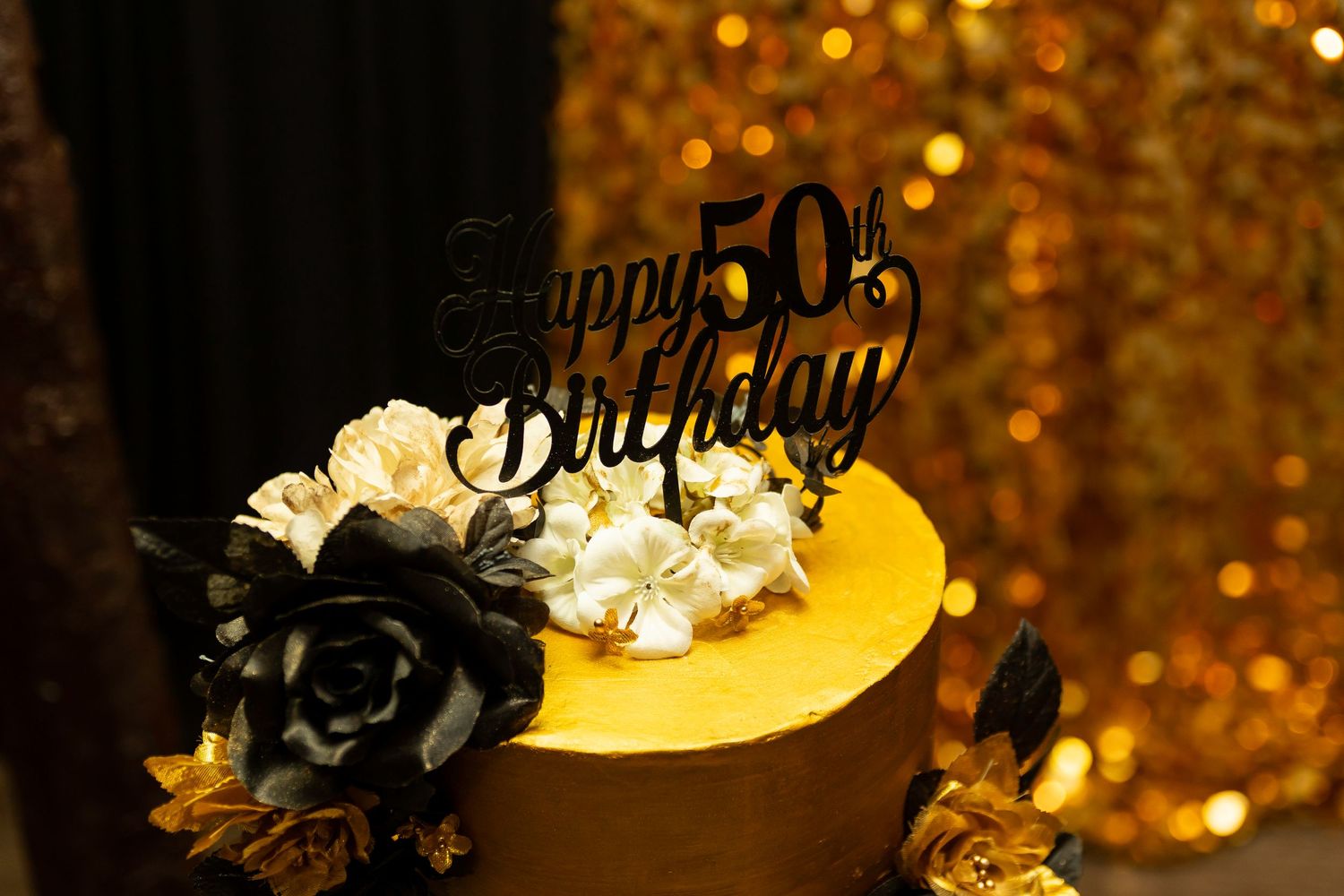 Happy 50th birthday cake decorated with black and white roses against a golden backdrop.