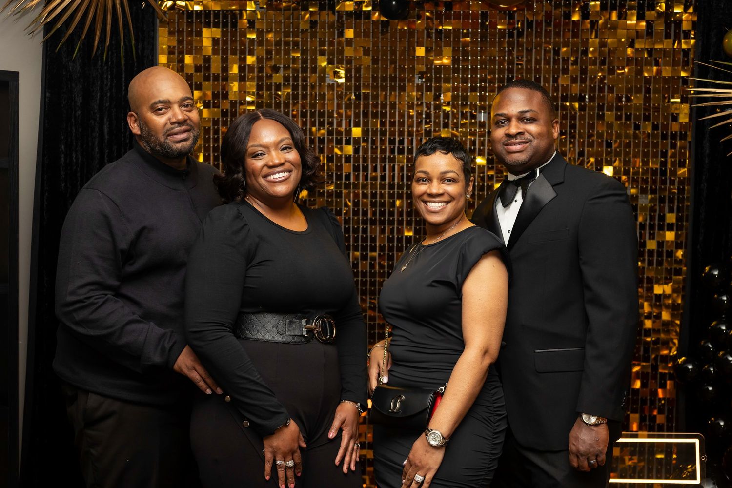 Party attendees gather for photos in front of a glittering gold backdrop with decorative accents.