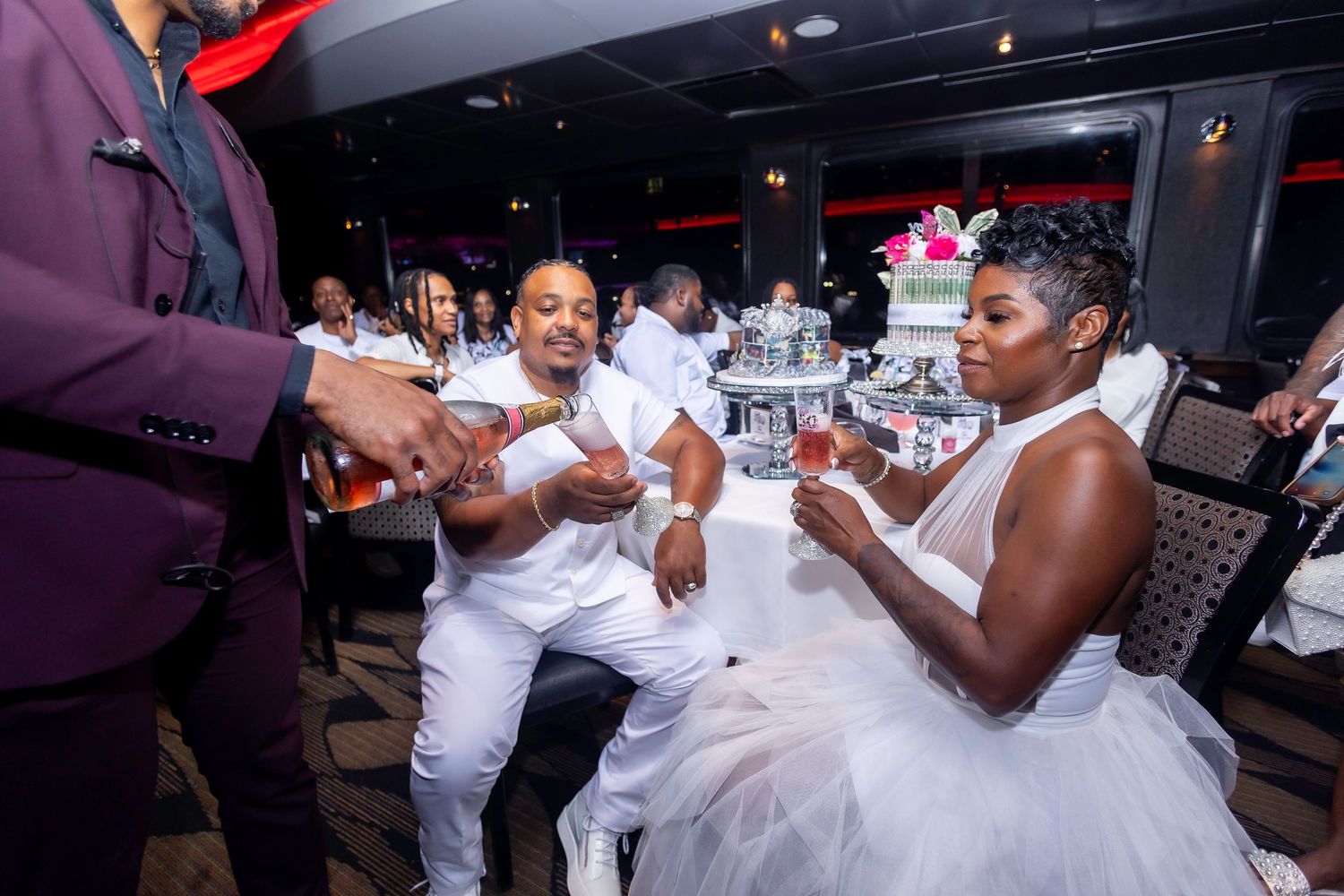 Guests in white attire socialize around a table during an evening celebration.