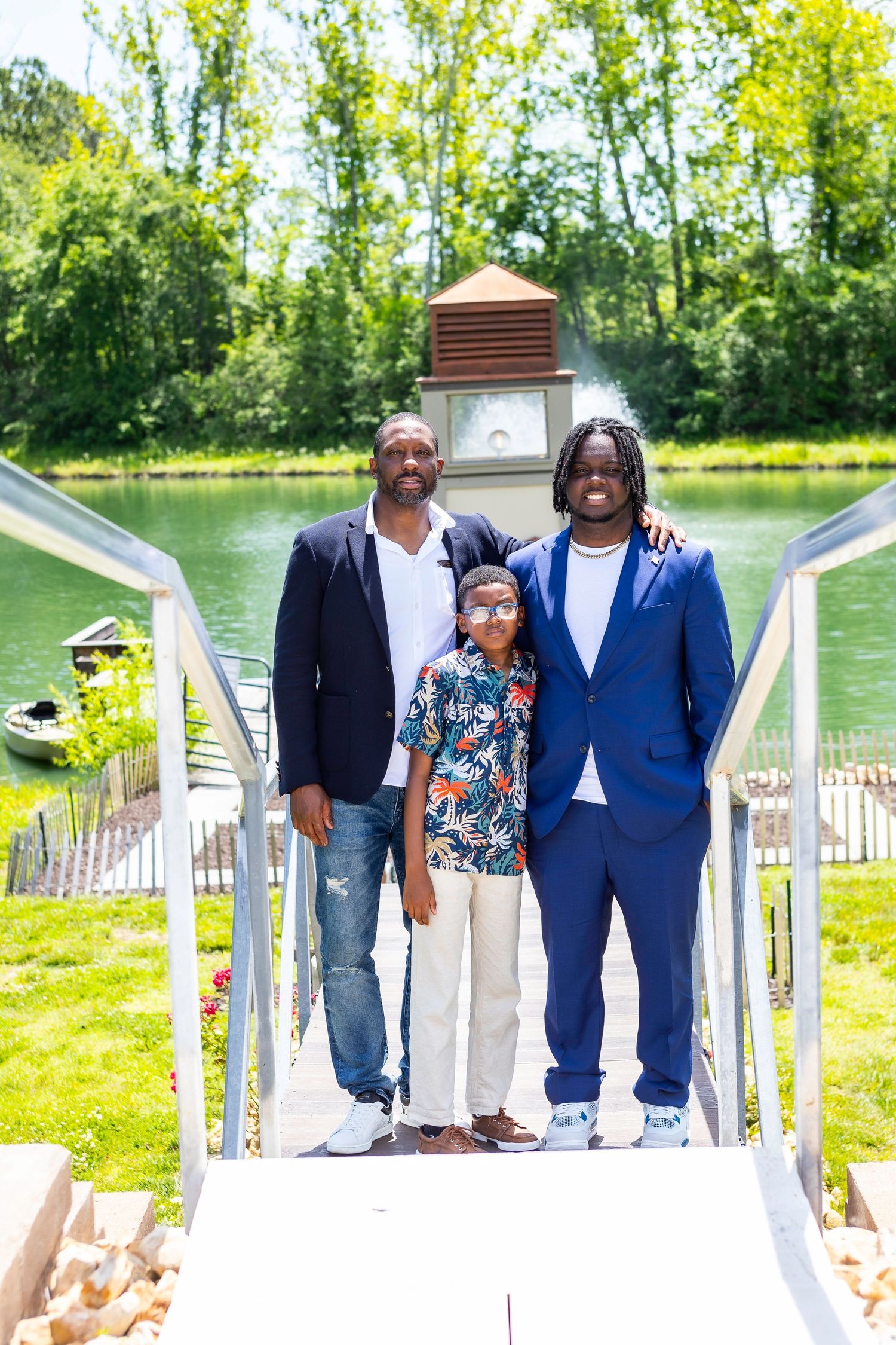 Family of three poses on a white bridge with a lake and fountain in the background.