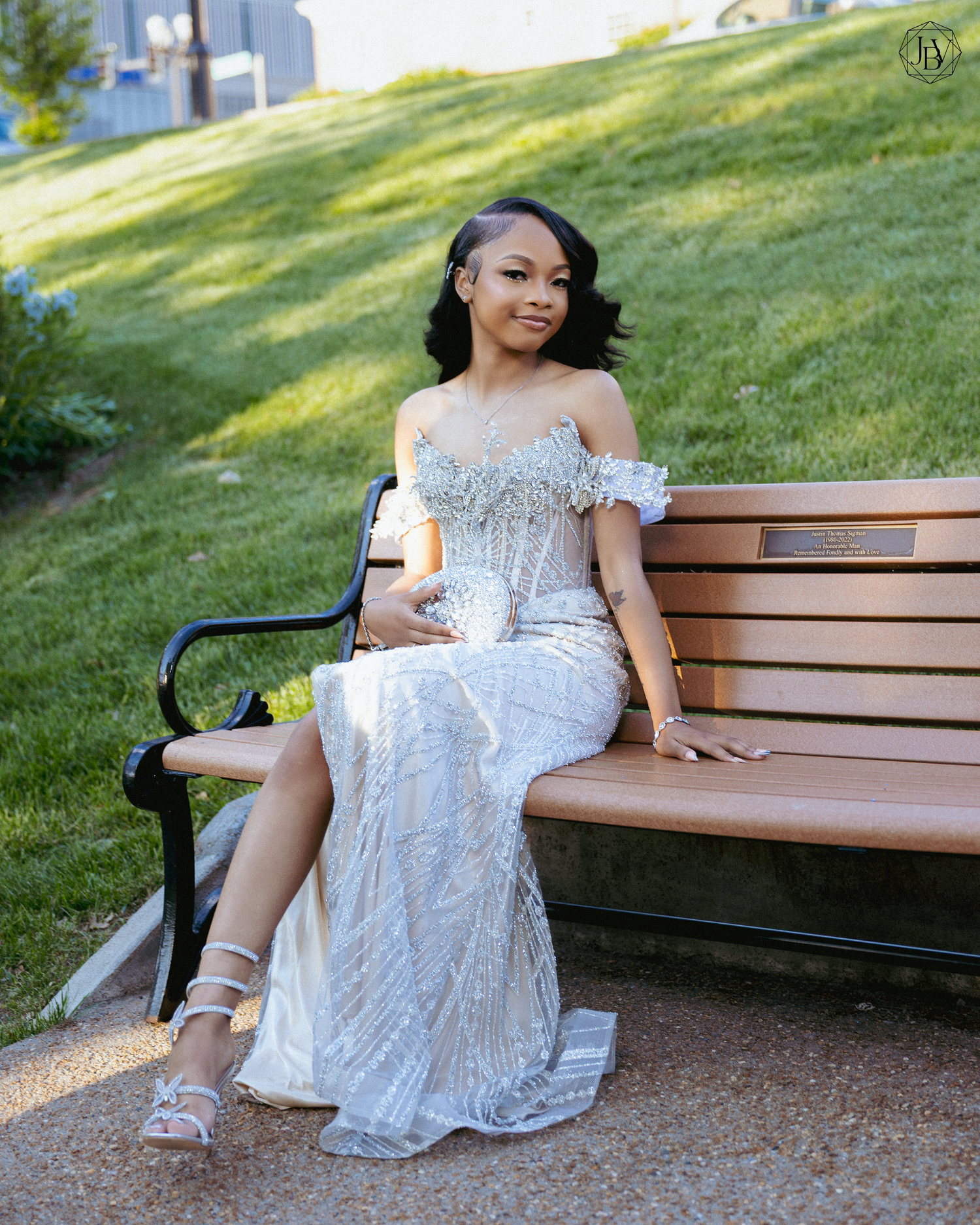 Young woman in elegant silver sequin gown seated on a park bench, posing gracefully for a formal occasion.
