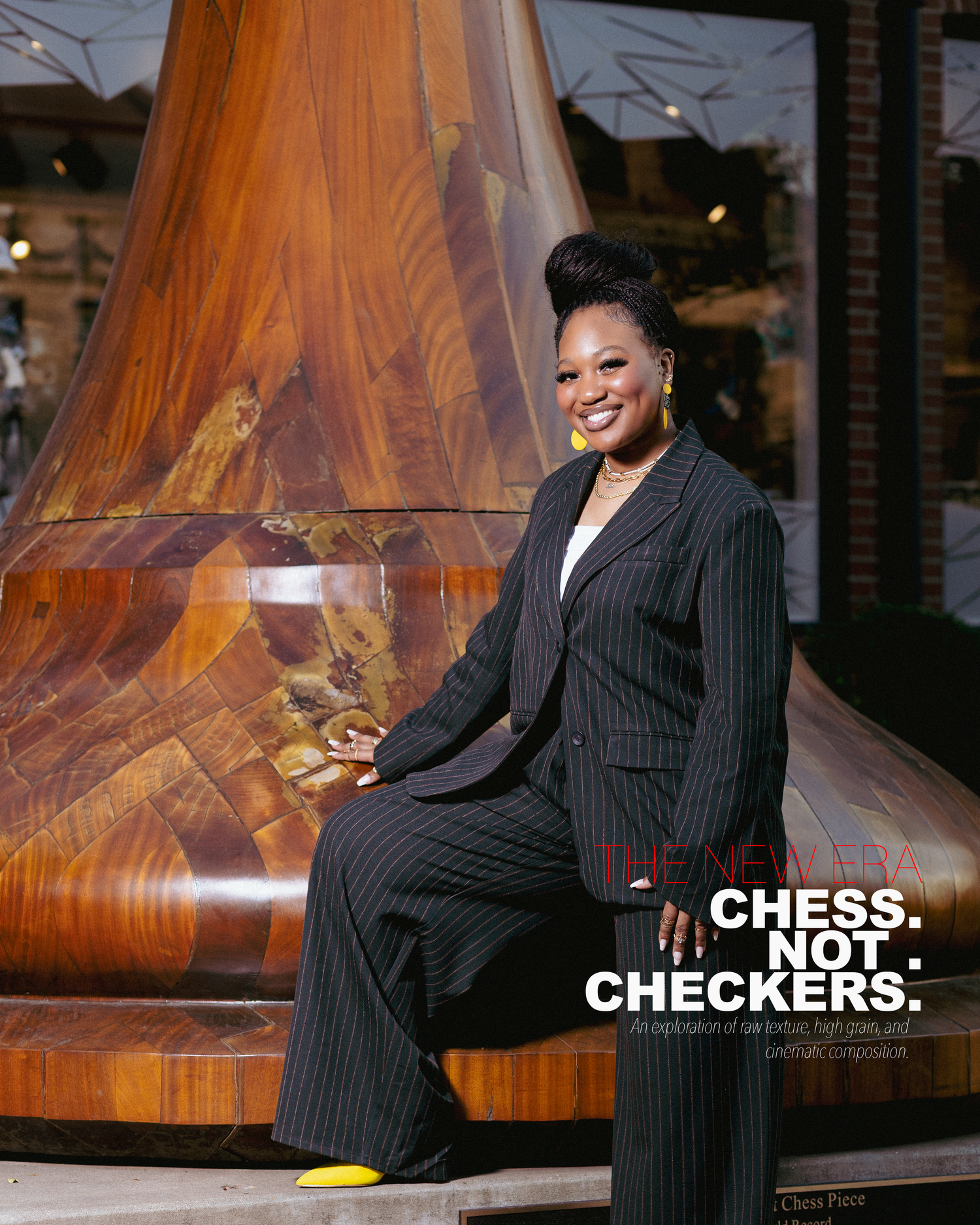 Woman in pinstripe suit smiling, seated near wooden sculpture, with Chess Not Checkers text overlay.