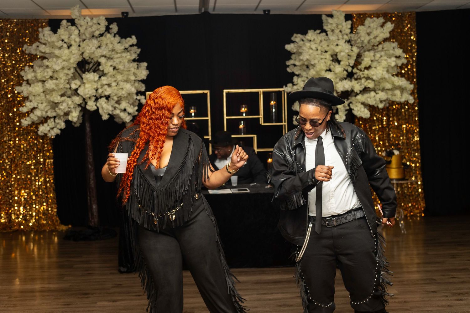 Two guests dancing energetically at a formal event with white floral arrangements.