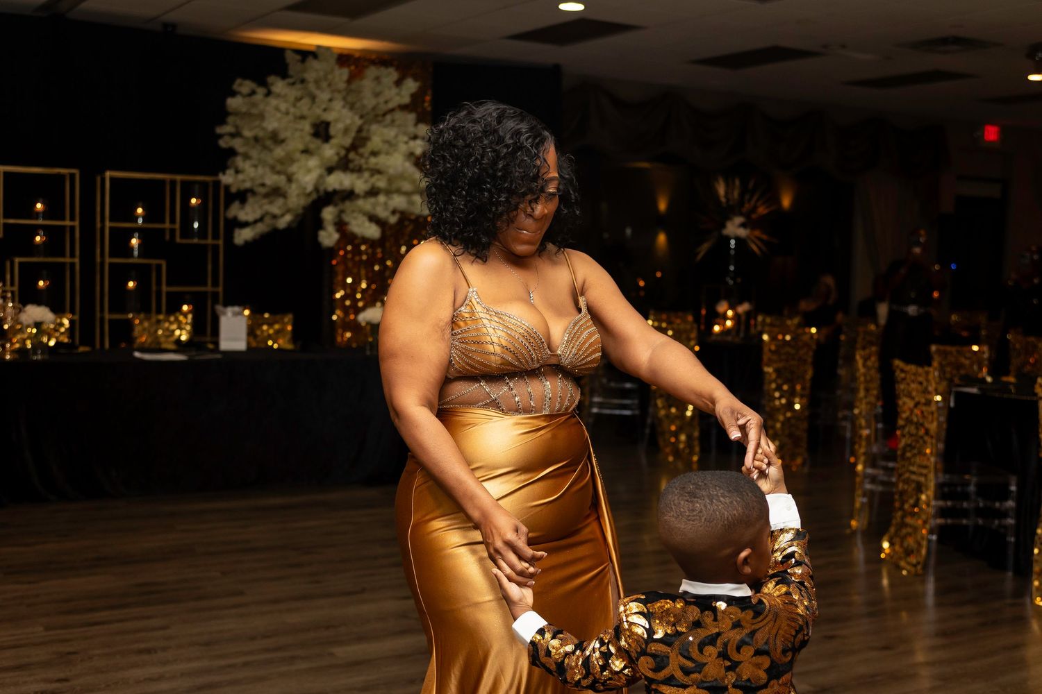 People celebrate at an elegant evening event with gold decor and balloons in the background.