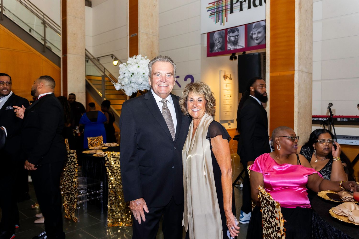 Guests mingle at an elegant evening event with gold decorative accents and ambient lighting.
