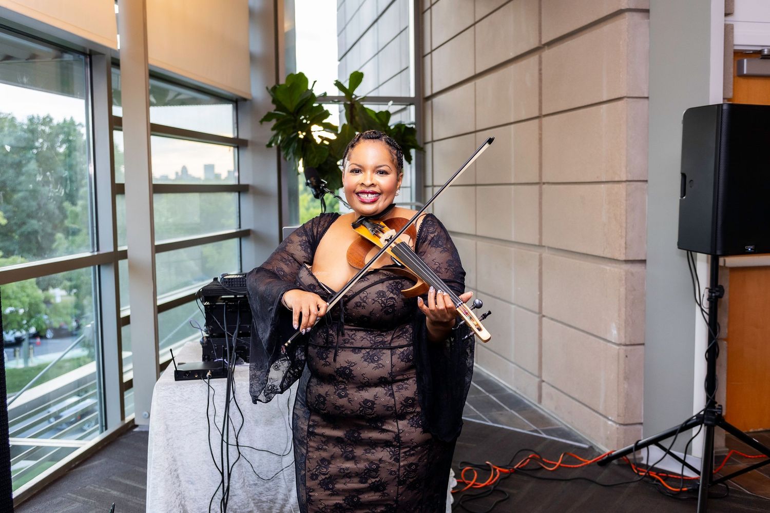 A musician performs with a violin in front of large windows during an indoor event.