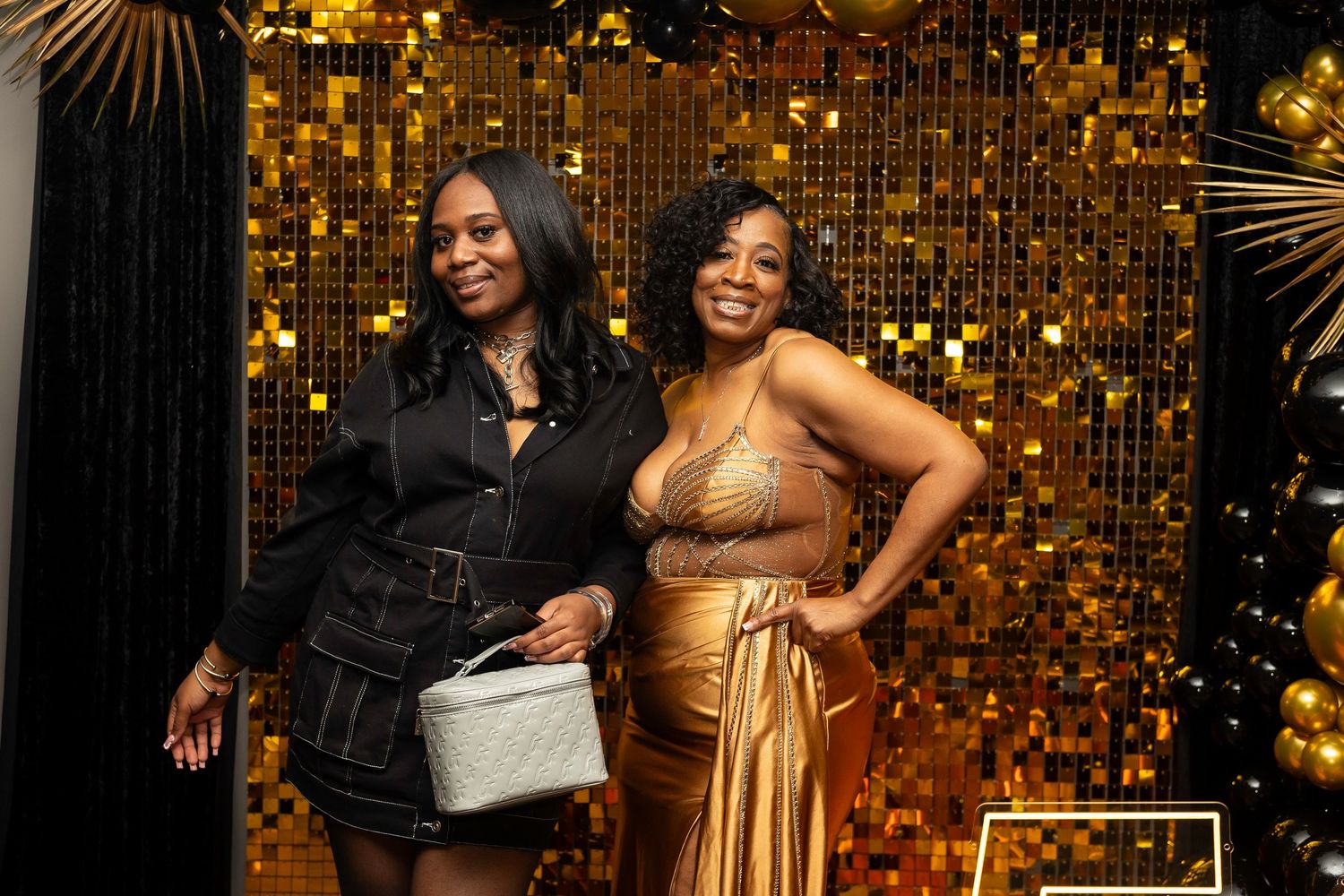 Partygoers pose by a glamorous gold balloon wall at an upscale evening celebration.