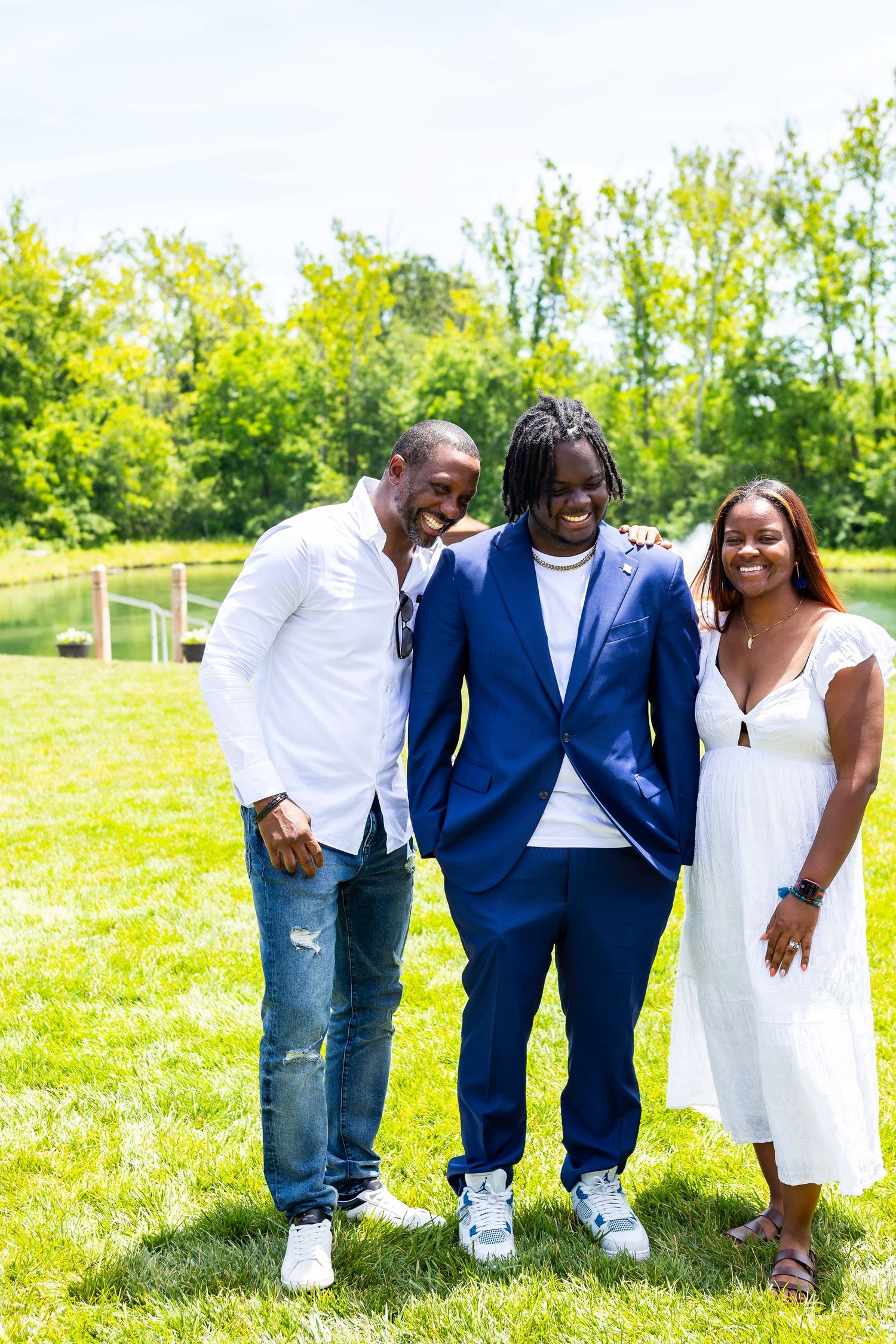 Three people dressed in stylish outfits pose together on a sunny day in a green outdoor setting.