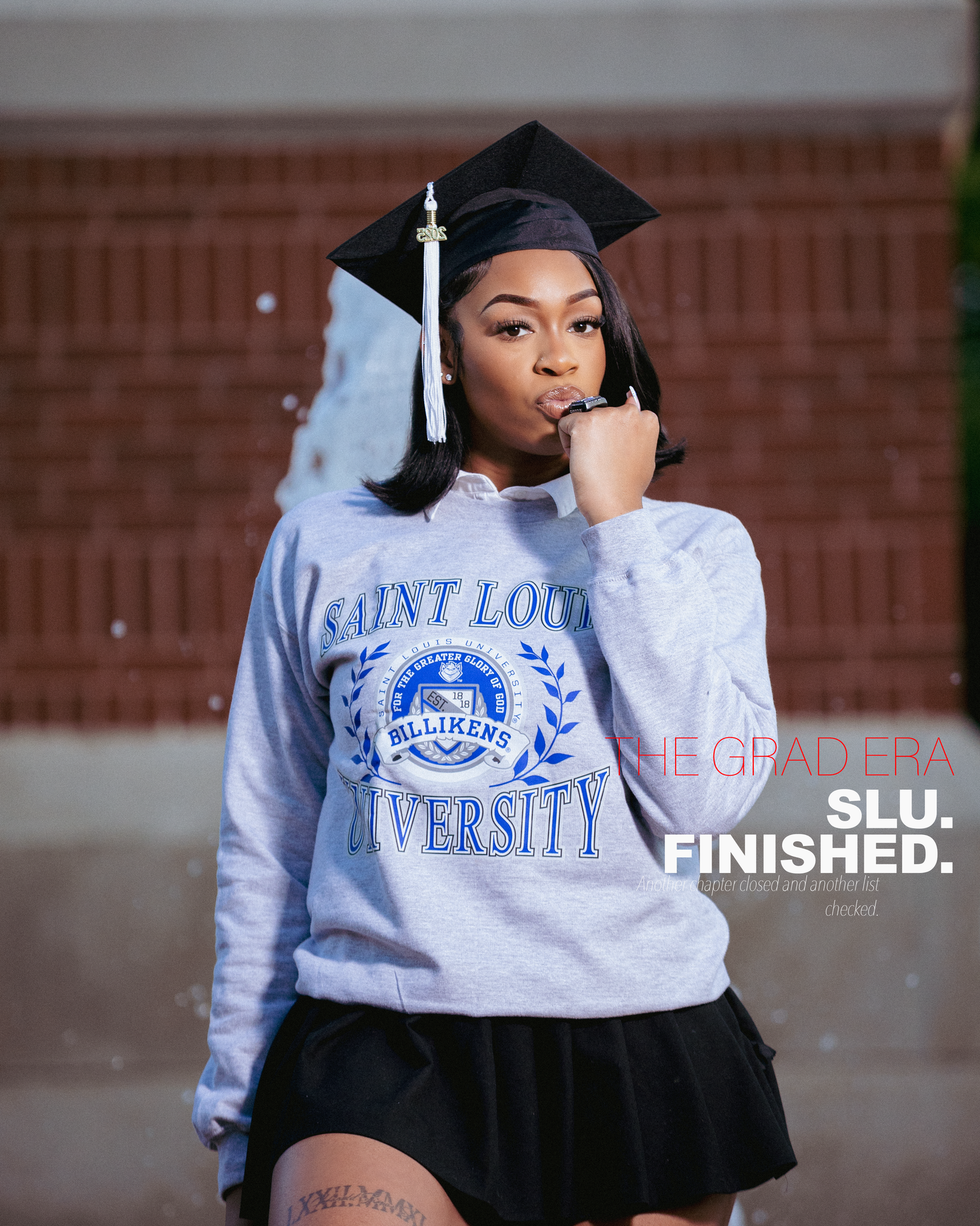Saint Louis University graduate posing in SLU sweatshirt and graduation cap celebrating completion of degree.