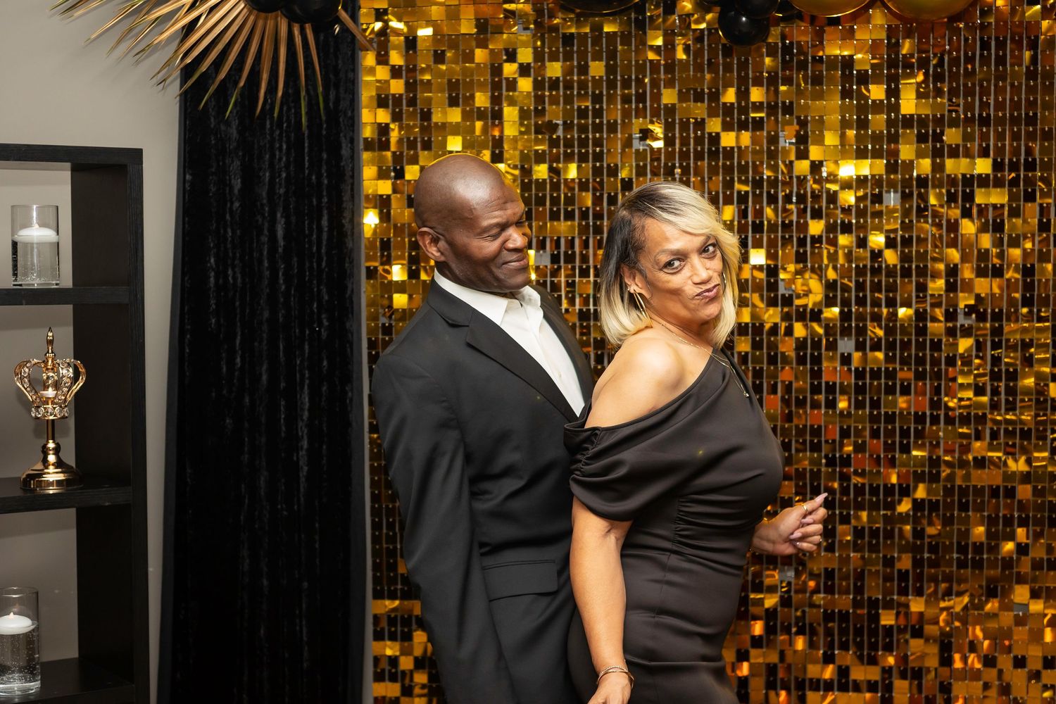 Couple posing together against a sparkling gold backdrop at an elegant event.