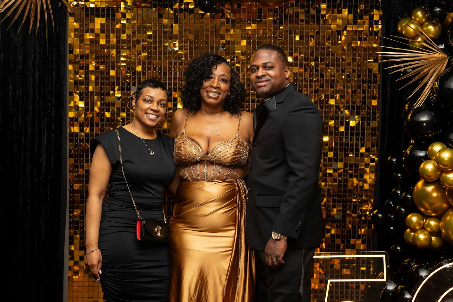 Guests celebrate at a formal event with a stunning gold balloon and palm leaf backdrop.